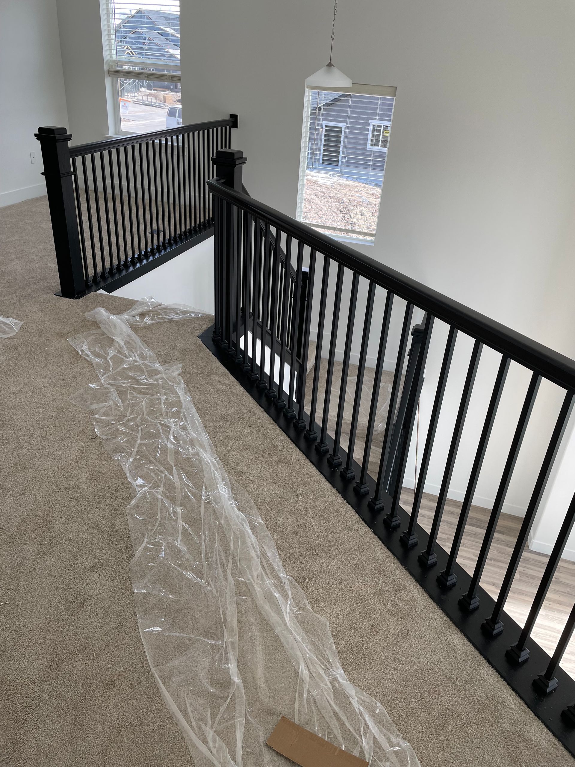 Black stair railing, carpeted landing, high window, and overhead light fixture.