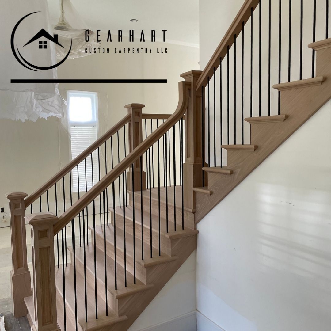 Wooden staircase with black metal balusters and wood handrails, inside a home.