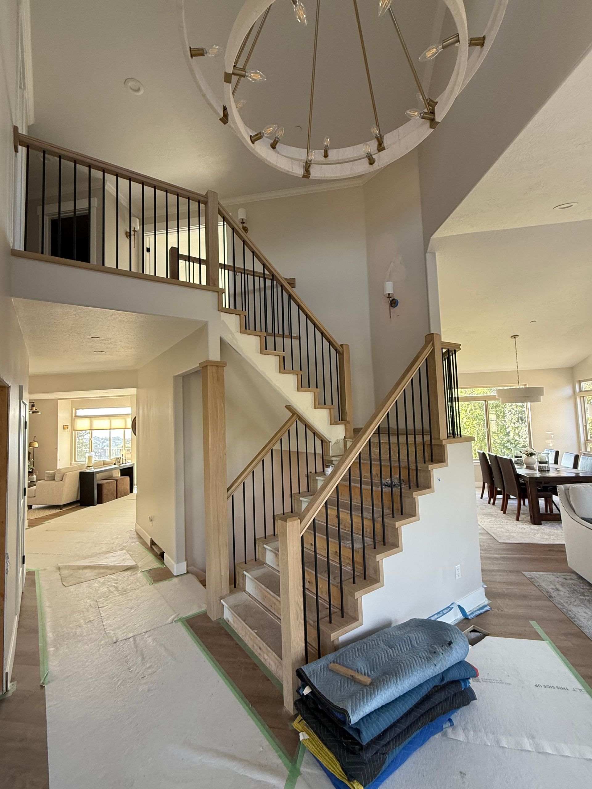 Two-story foyer with a wooden staircase and black iron balusters. A circular chandelier hangs above.