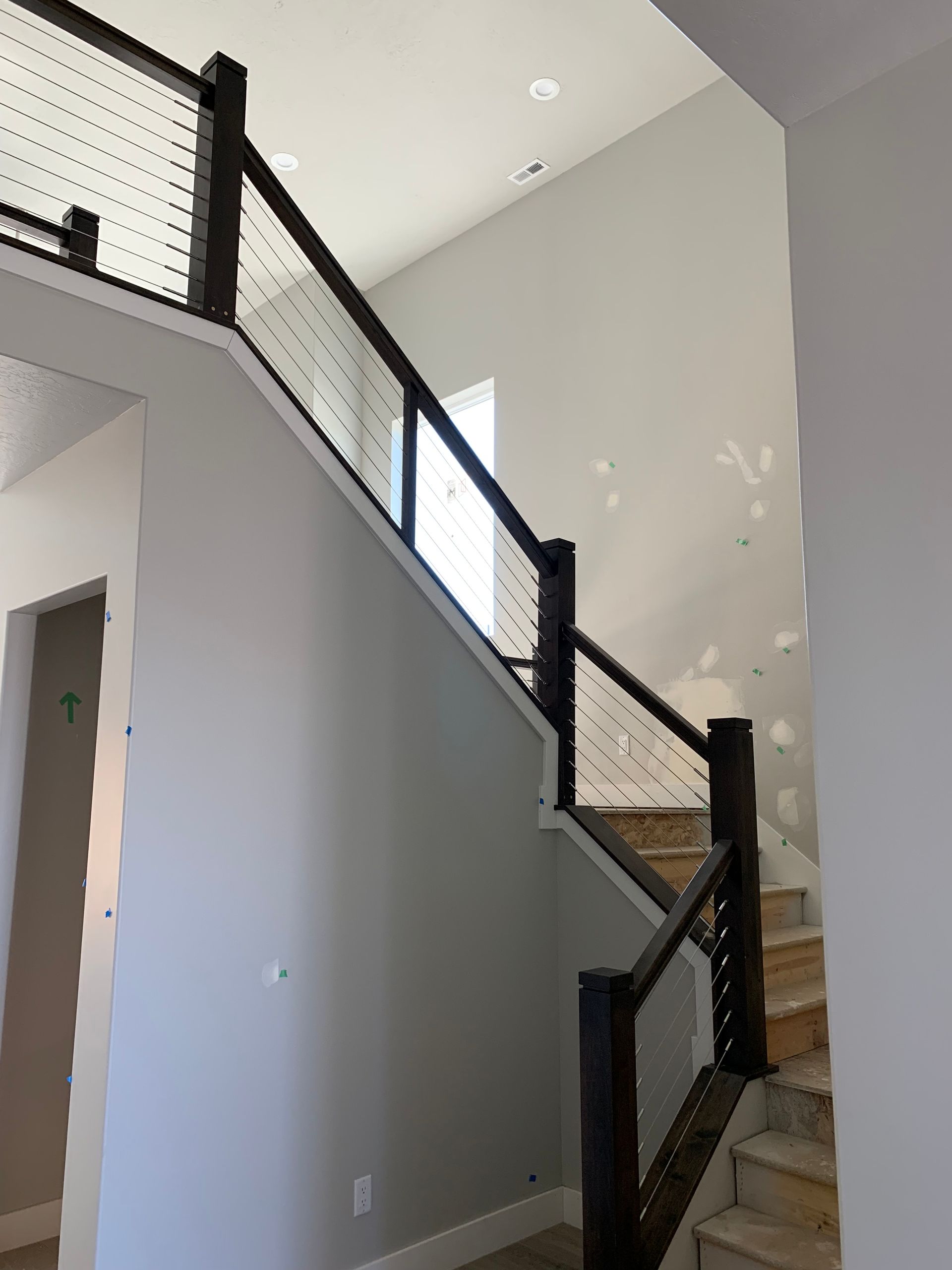 Staircase with dark wood railing and metal cable infill, ascending a light gray wall.