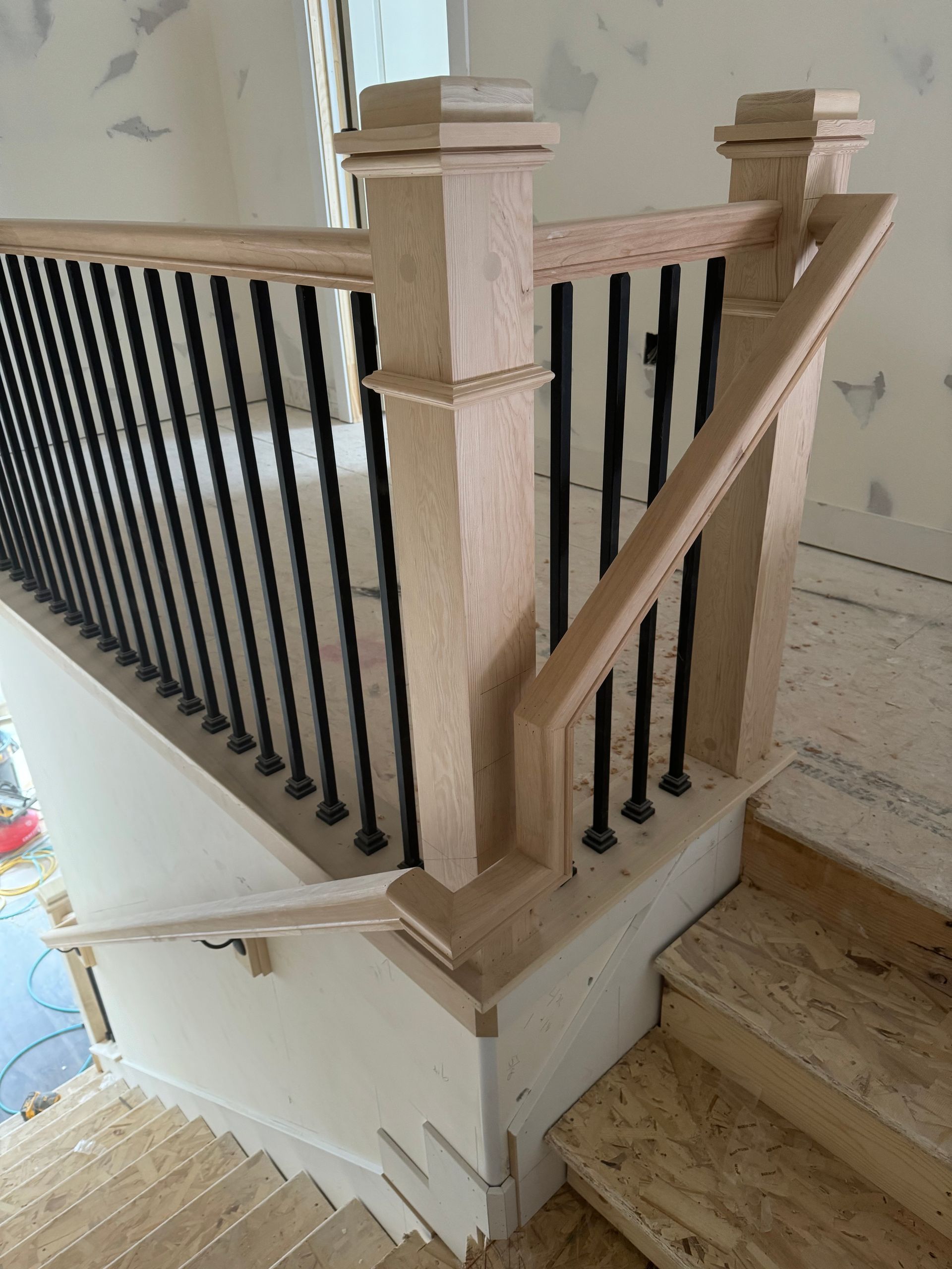 Wooden staircase with black metal balusters and light-colored newel posts, indoors during construction.