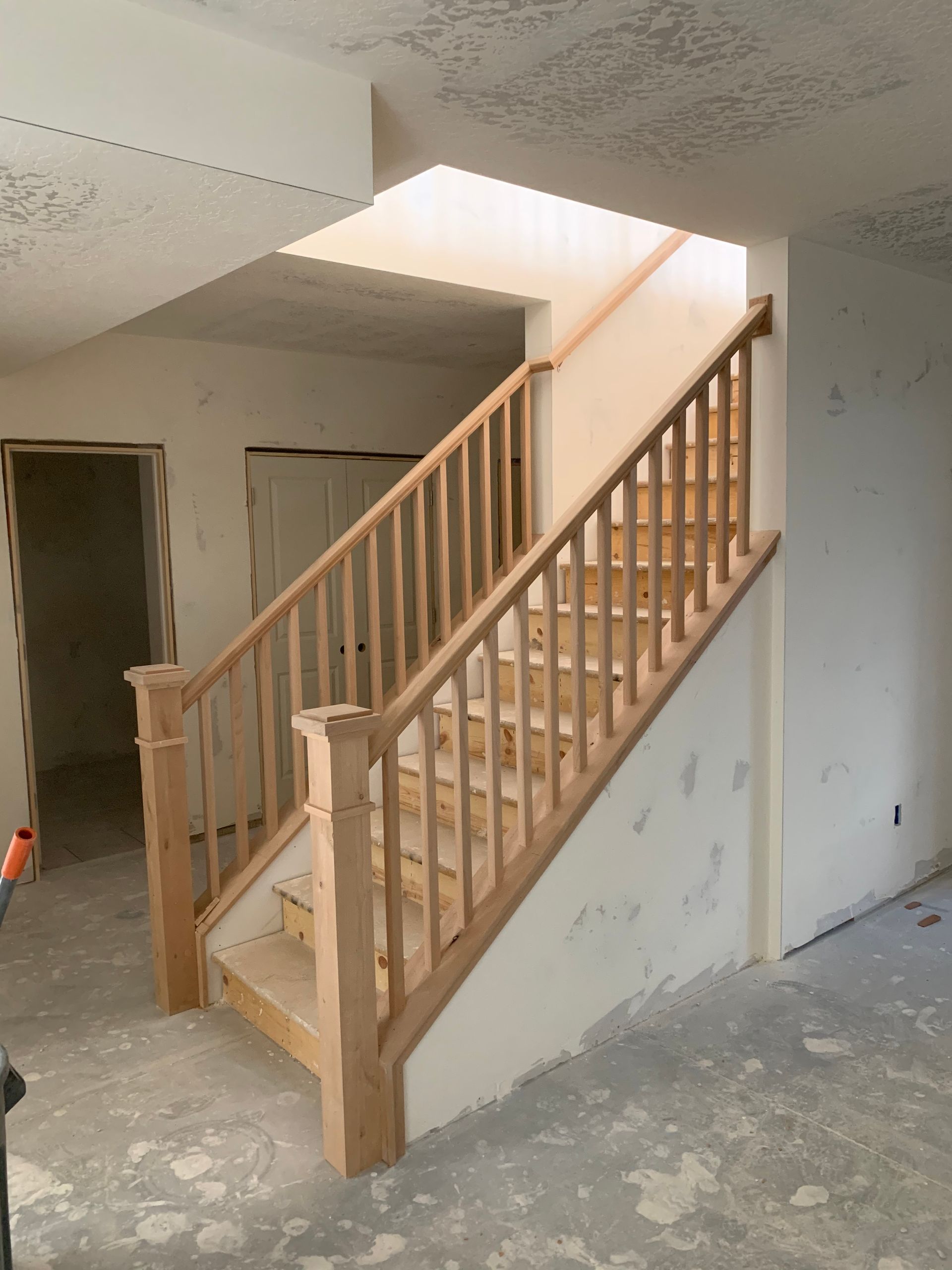 Wooden staircase in a home under construction. Includes handrails and balusters. White walls, concrete floor.