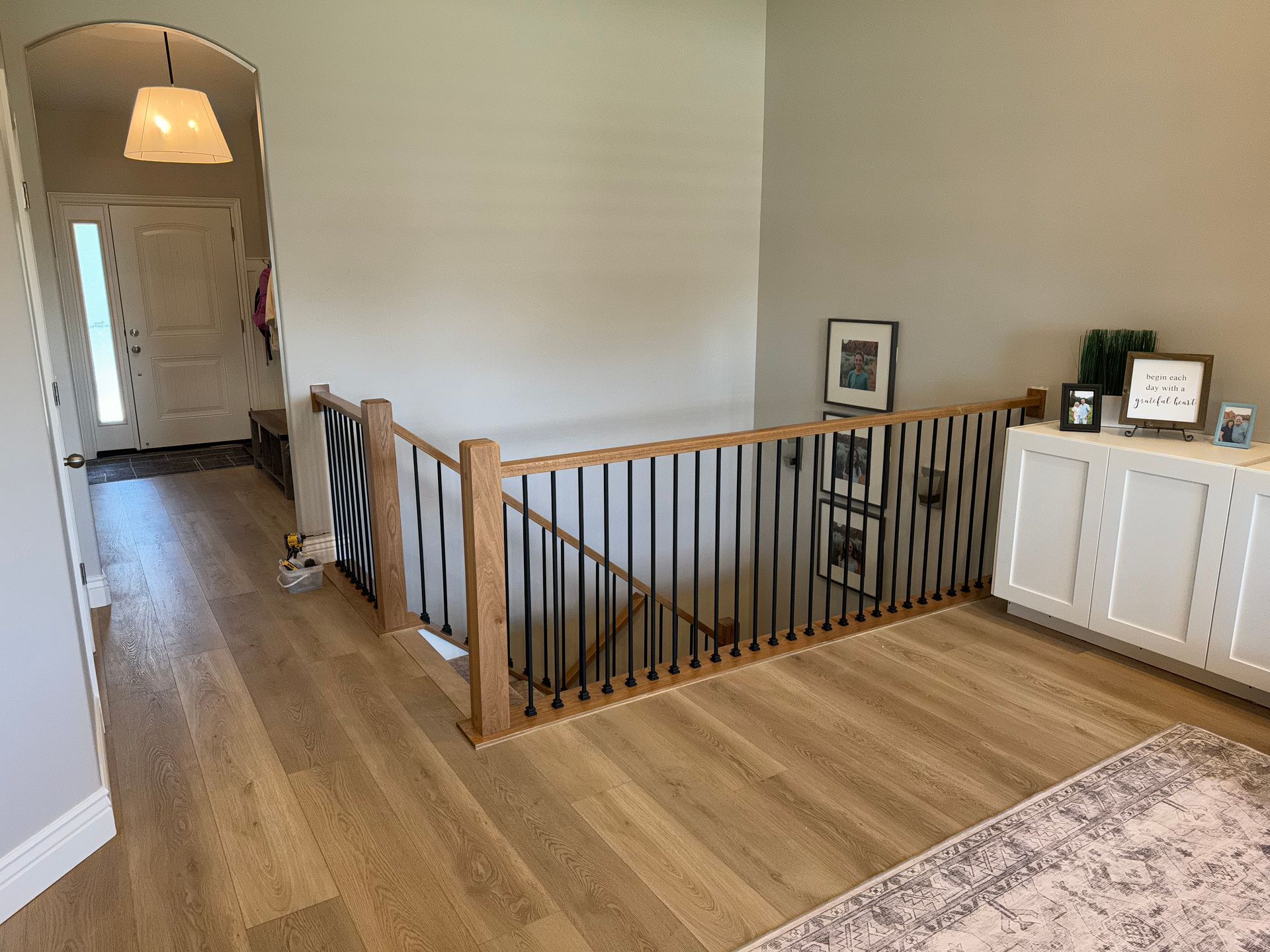 Hallway with light wood floors, a staircase with black railings, and a white cabinet with decor.