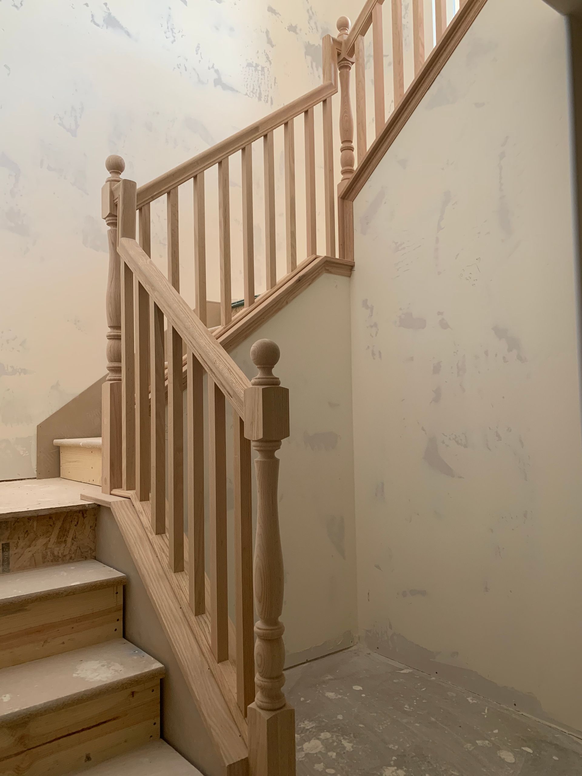 Wooden staircase with spindles and handrail, unfinished, against pale walls, in a home.