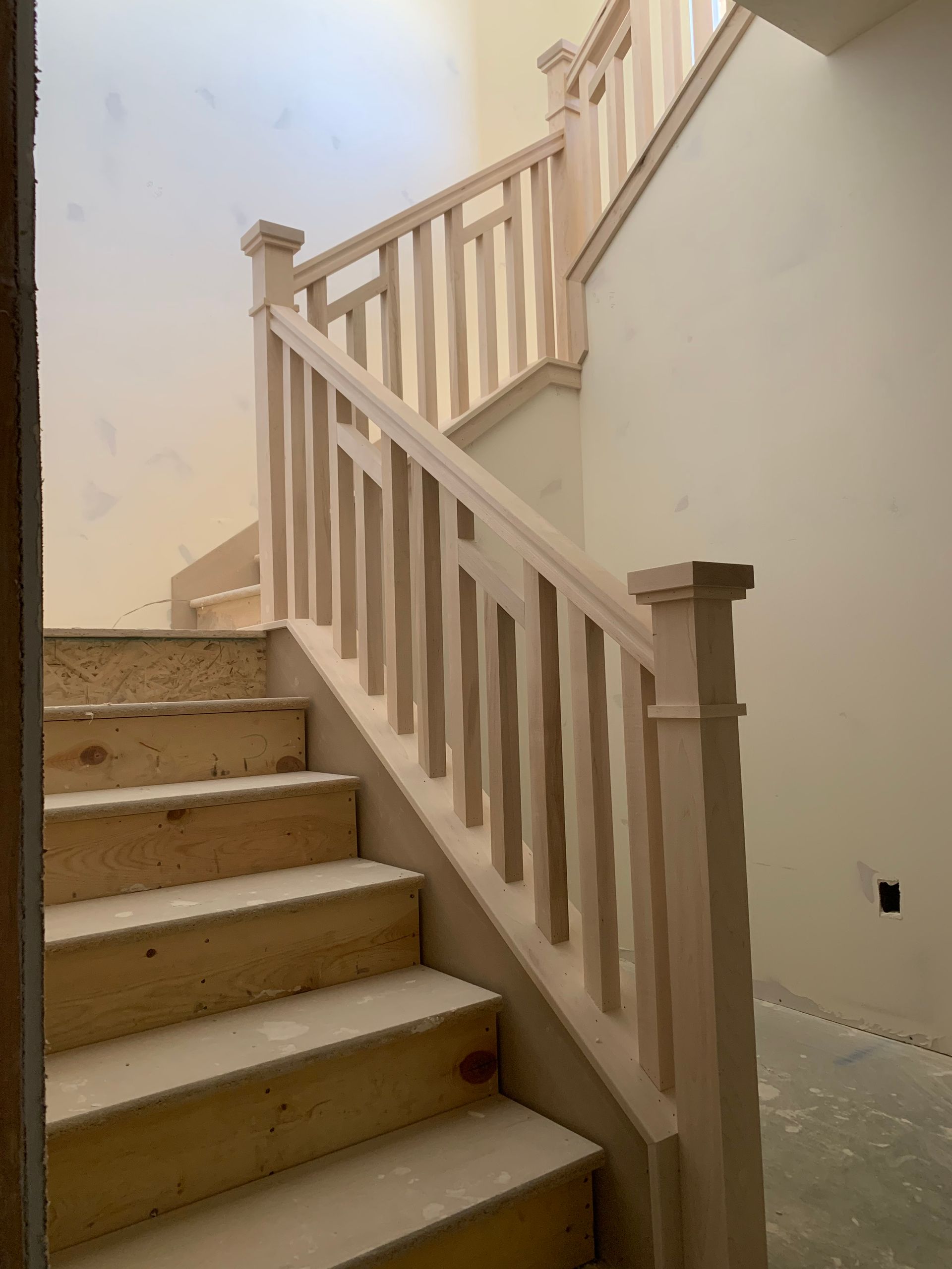 Wooden staircase with unfinished steps and railing against beige walls.