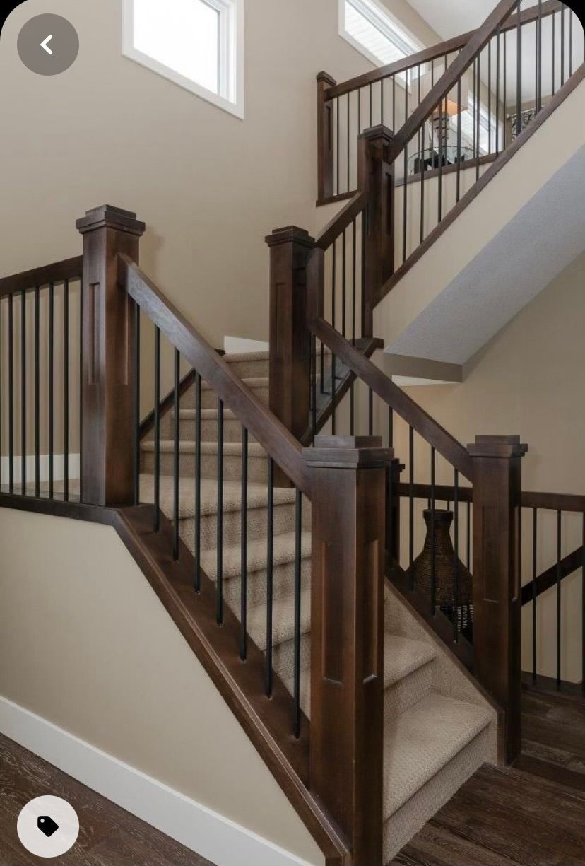 Wooden staircase with dark brown handrails, black spindles, and carpeted steps against beige walls.