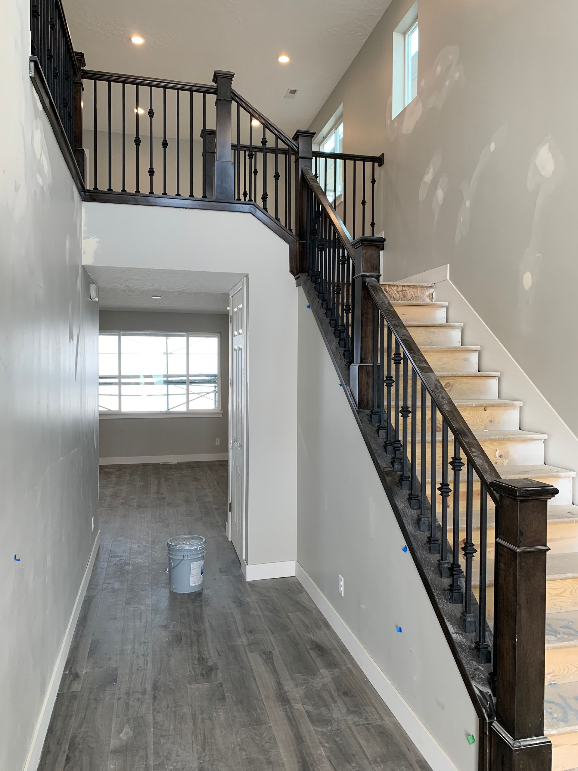 Interior view of a two-story home with a staircase, dark railing, light gray walls, and gray flooring.