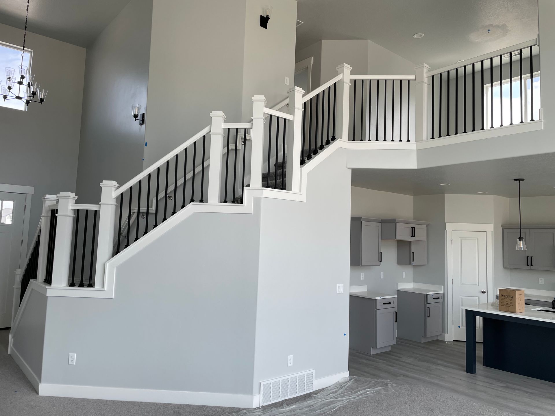 Two-story interior with staircase, black railings, white accents, and a kitchen with gray cabinets.