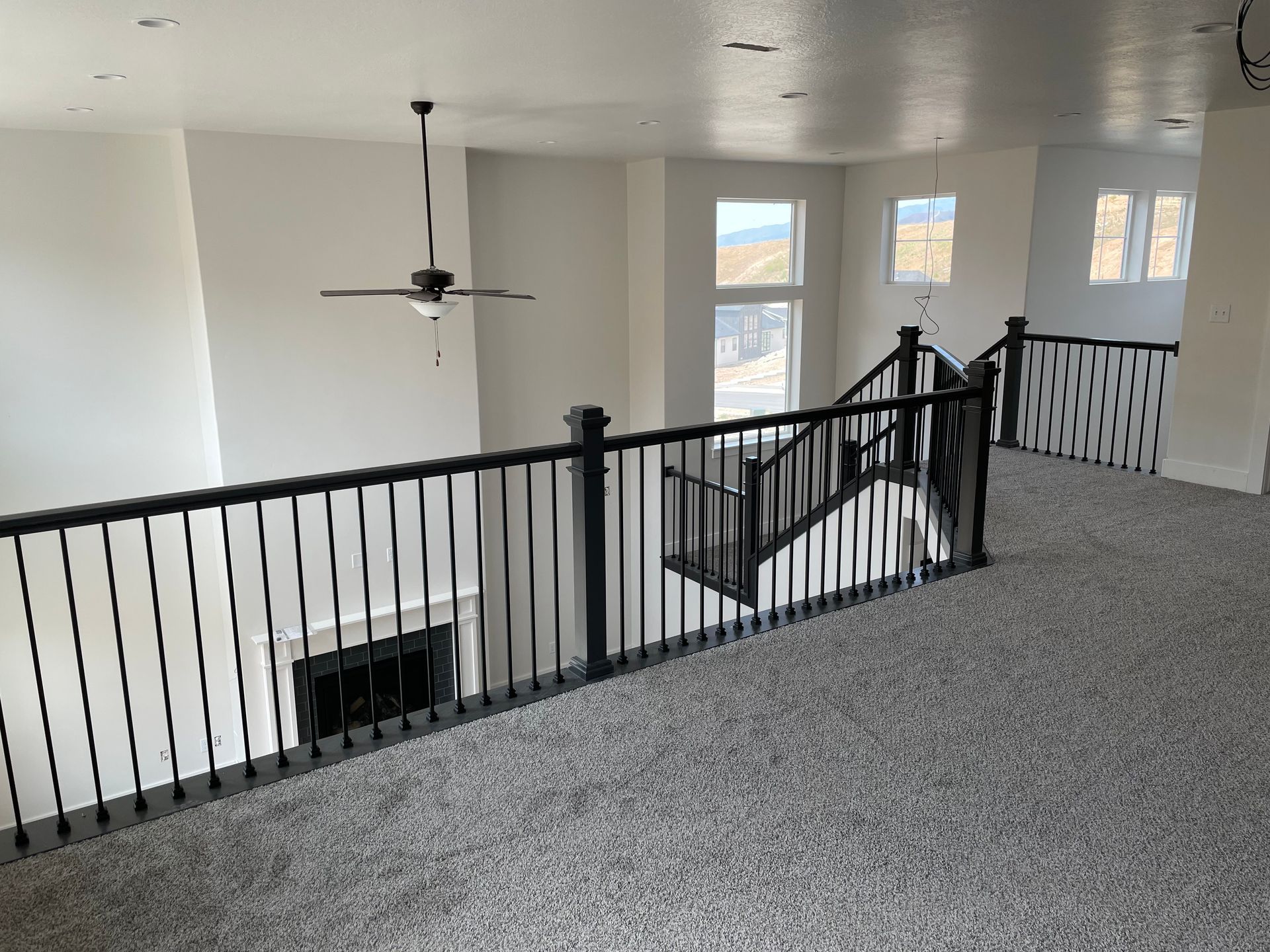 Interior of a home with a loft, black railing, fireplace, and carpet.