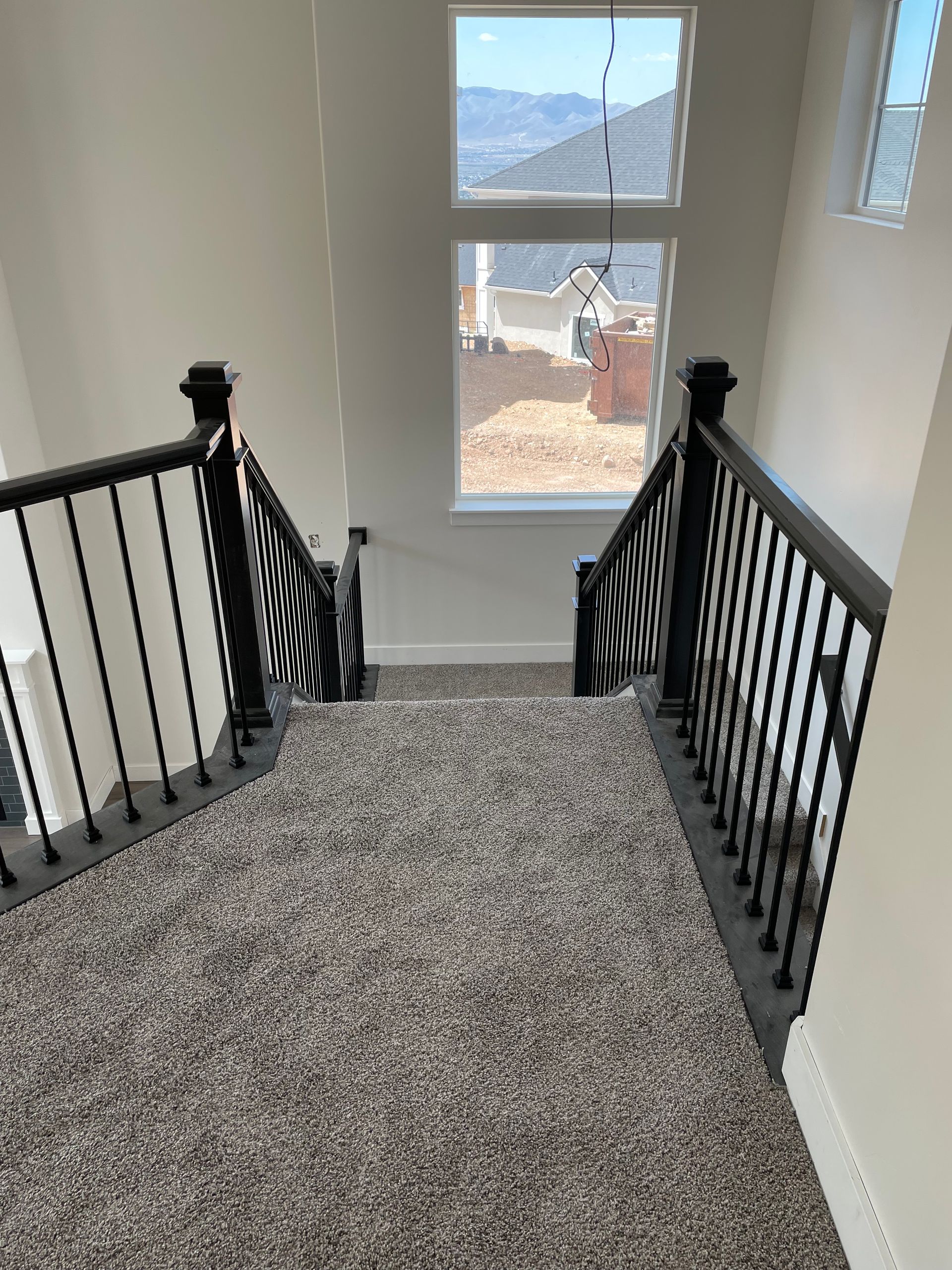 Staircase with black railing and carpet. Windows offer a view of the outdoors.