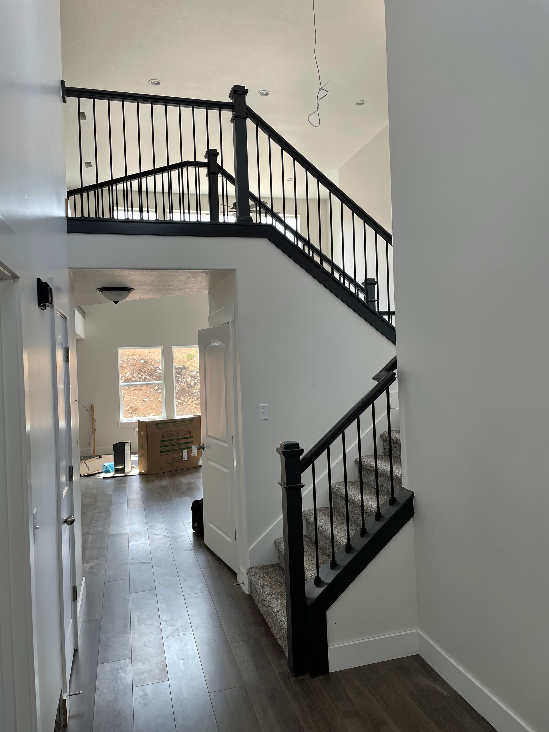 Hallway with stairs and black railing, leading to an upper level. White walls, wooden floor.