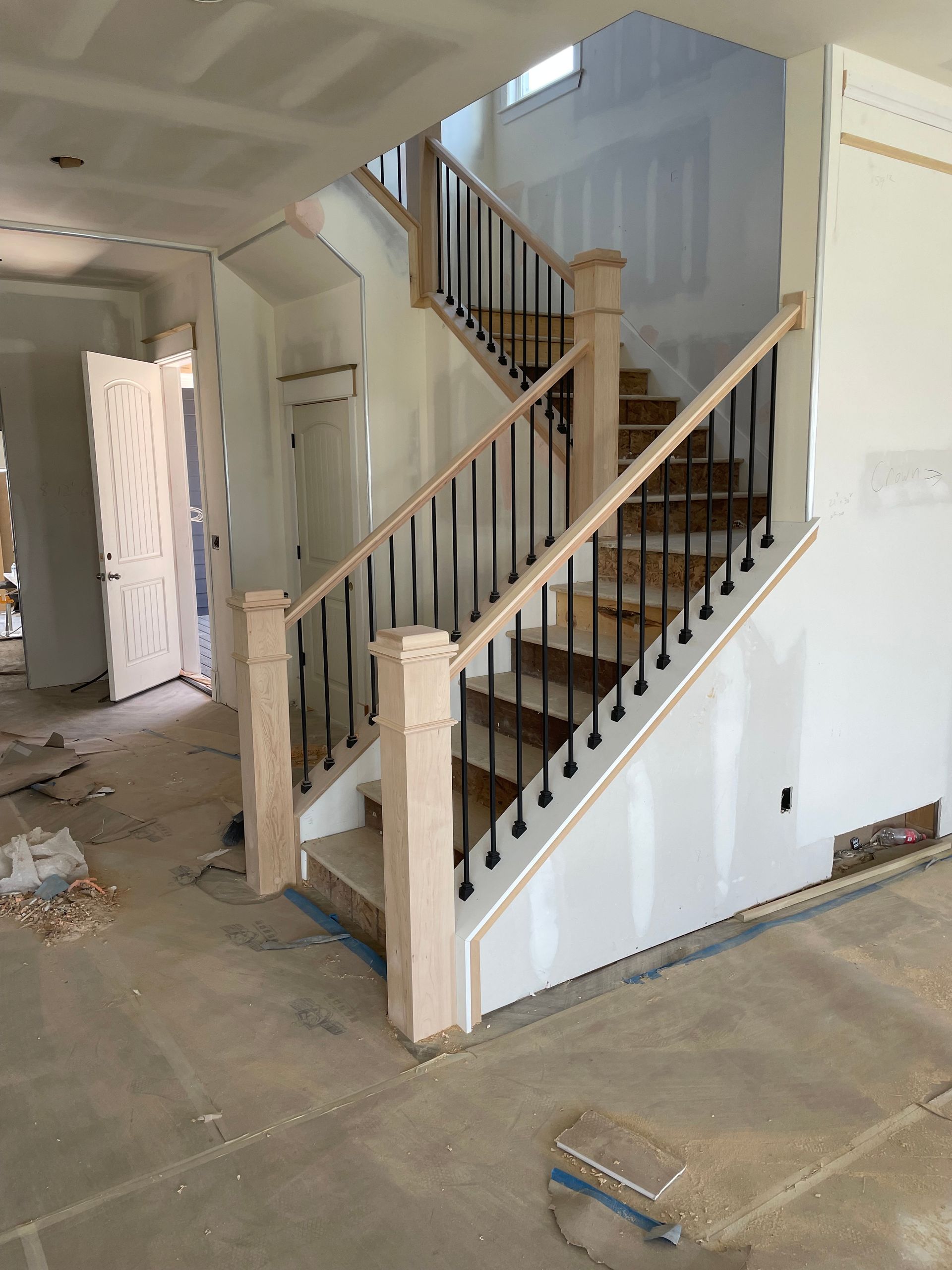 Interior view of a staircase during construction, with wooden steps, black iron balusters, and unfinished walls.