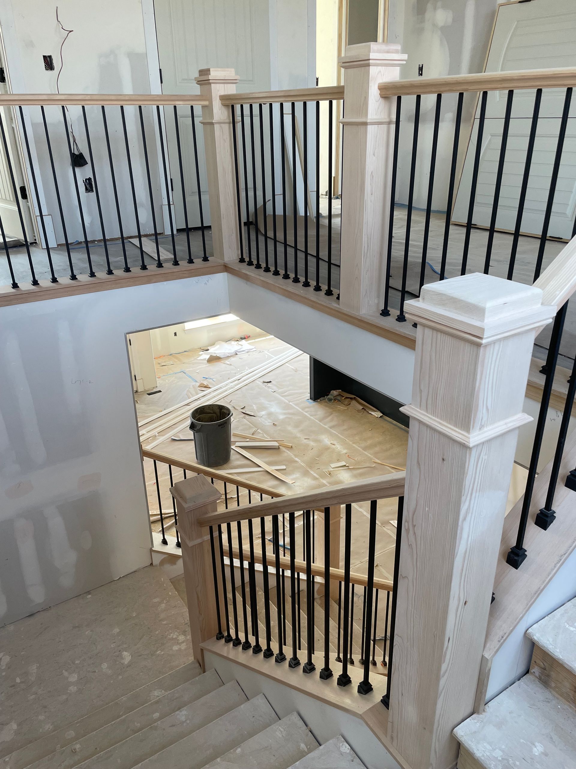 Staircase under construction: light wood railings, black spindles, open landing, unfinished walls and floor.