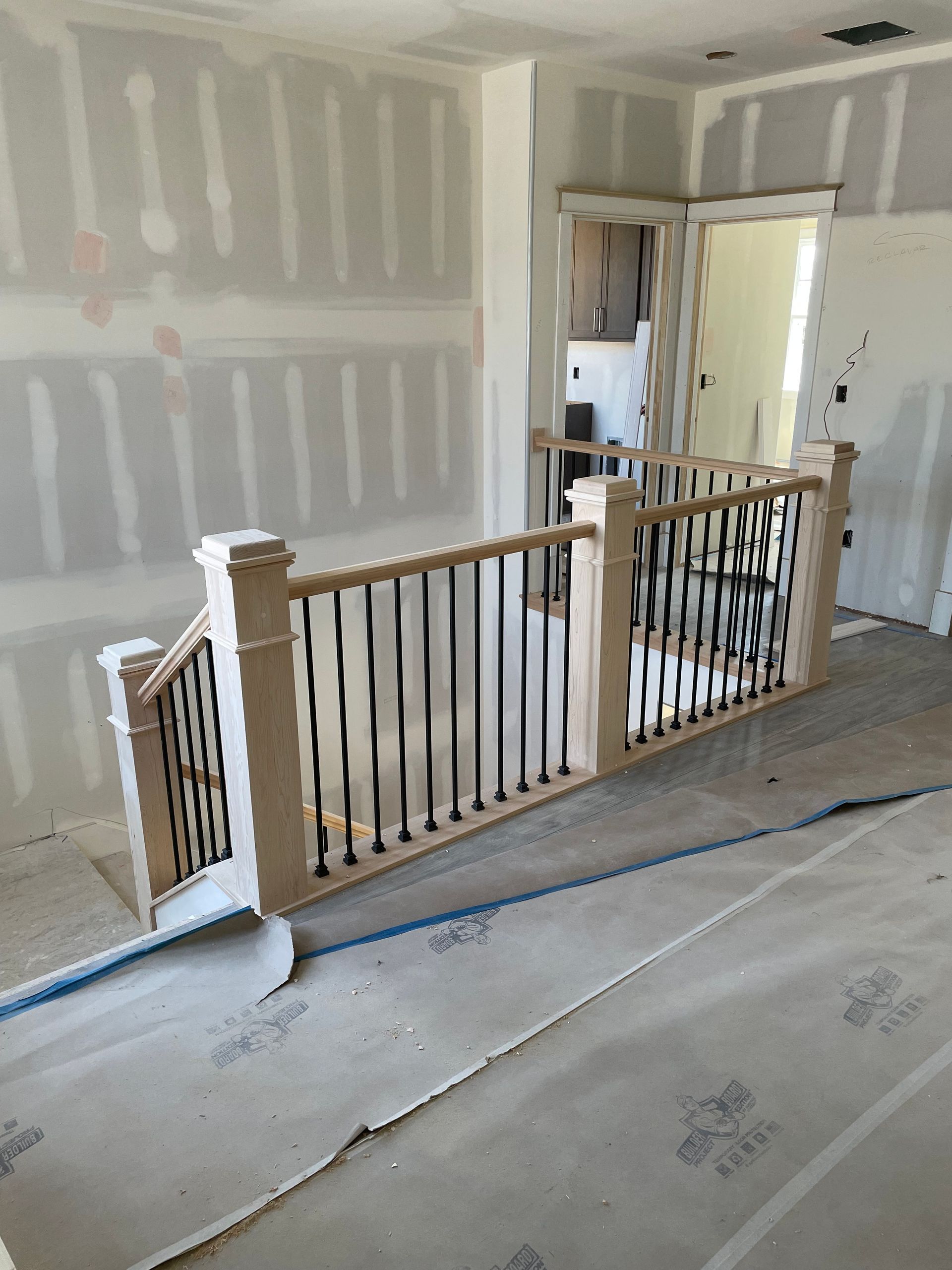 Staircase under construction with wooden railings and black vertical bars; doorway in the background.