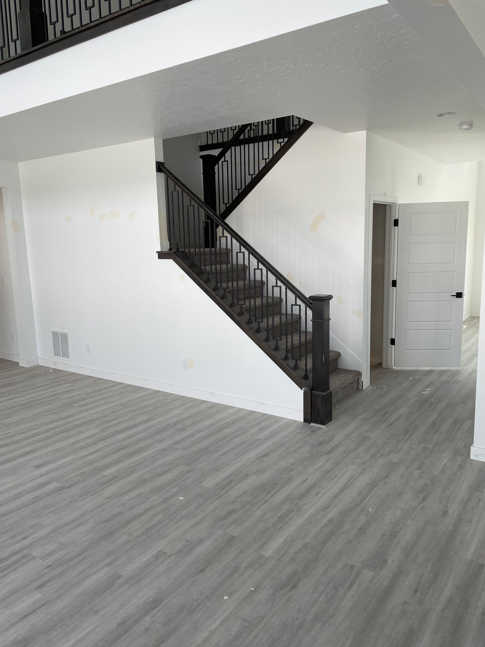 Interior view of a modern home with stairs, gray flooring, white walls, and a closed door.