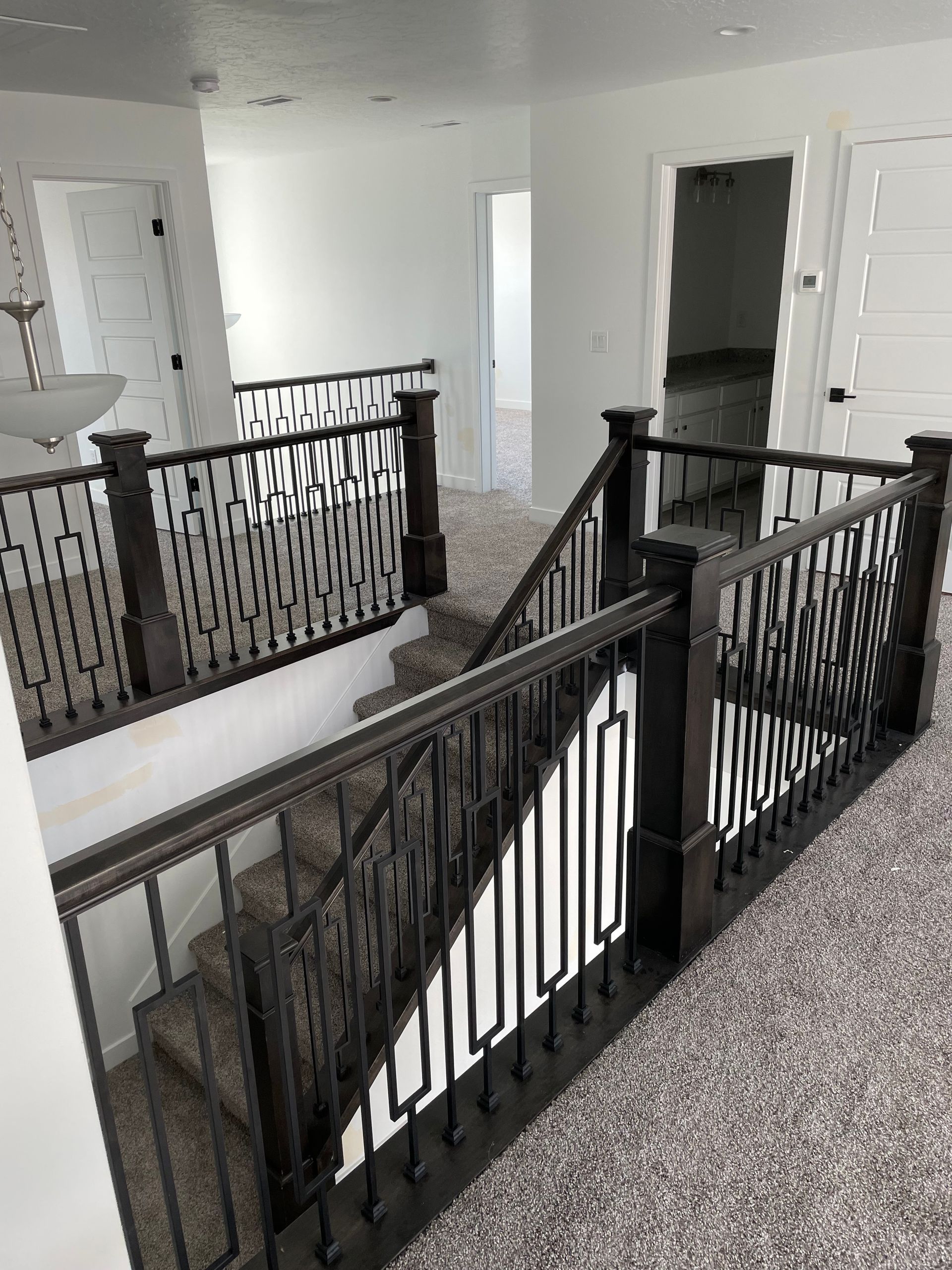 Interior view of a staircase with dark wood railings and patterned metal accents, leading to a hallway with white doors.