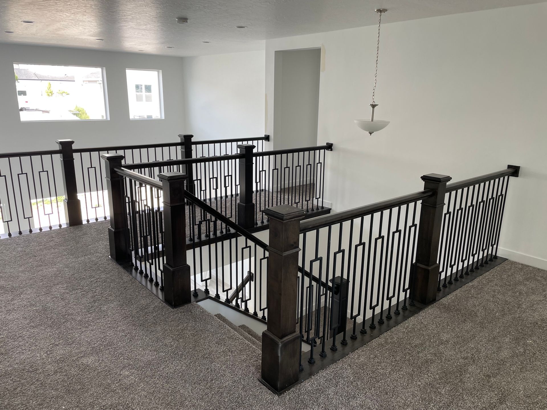Interior view of a second-floor hallway with carpet, dark railings, and a hanging light fixture.