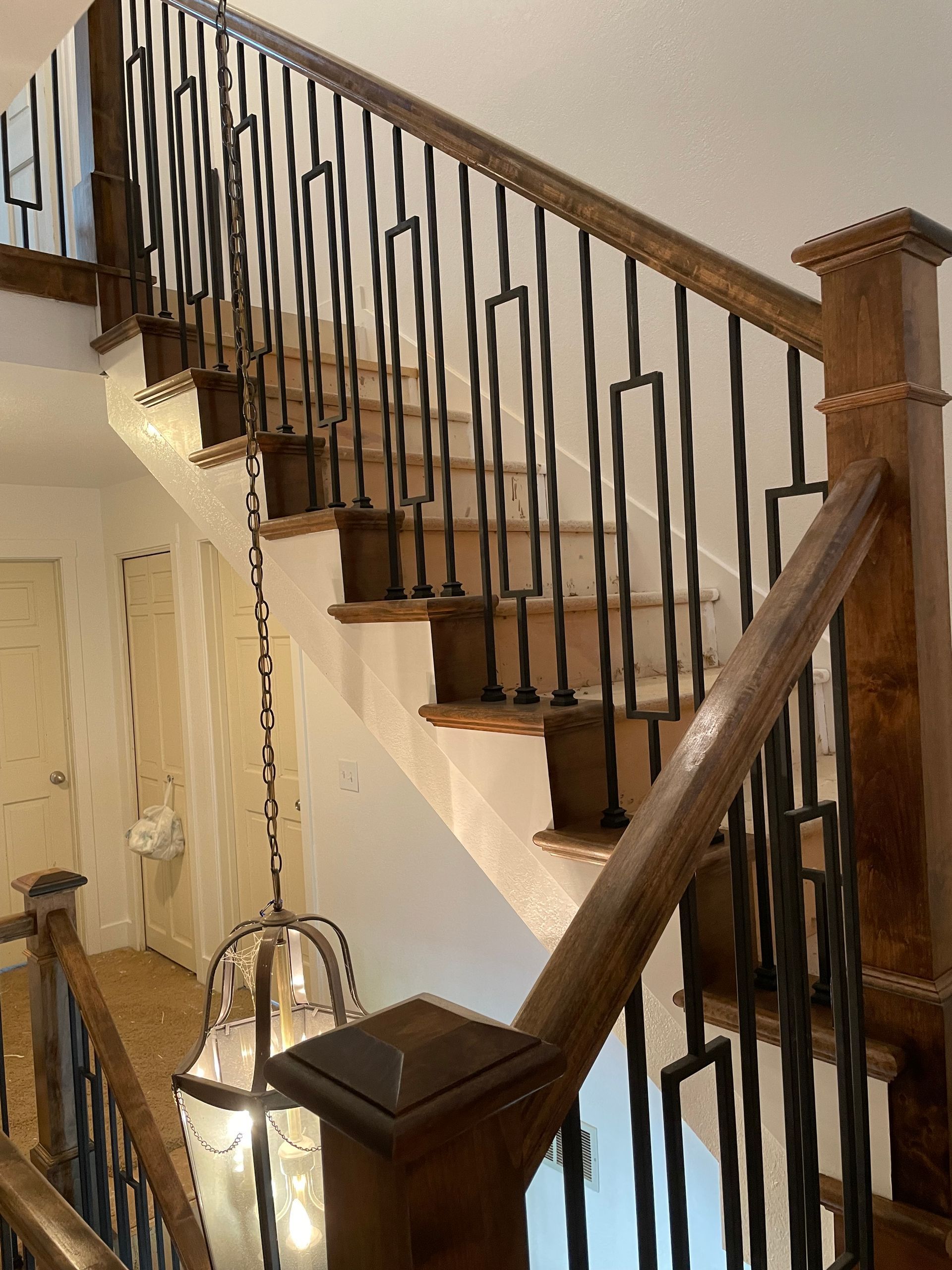 Wooden staircase with dark metal railings, chandelier, and stained wood accents.