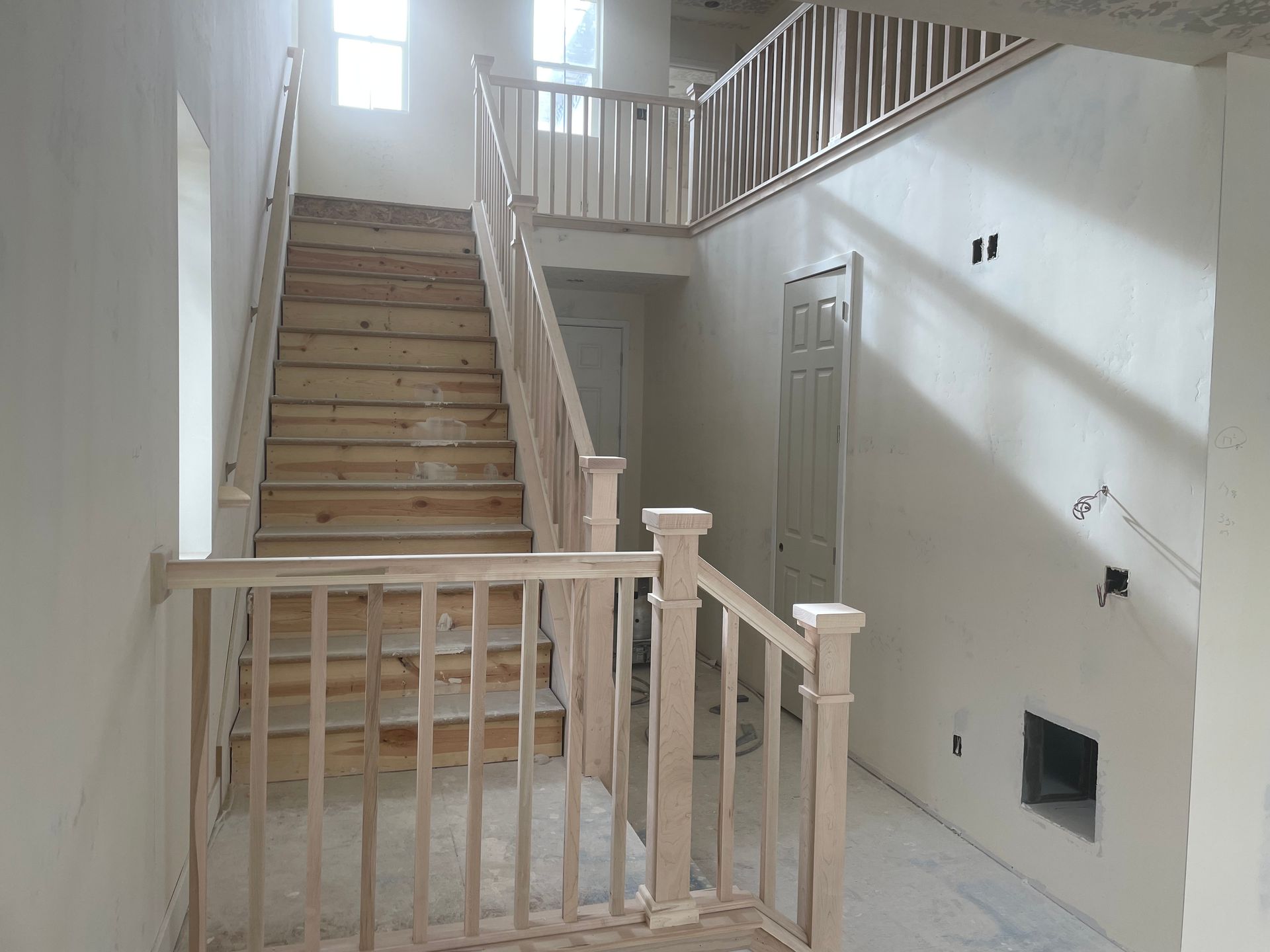 Interior of a building under construction, featuring a wooden staircase with railings and a landing area.
