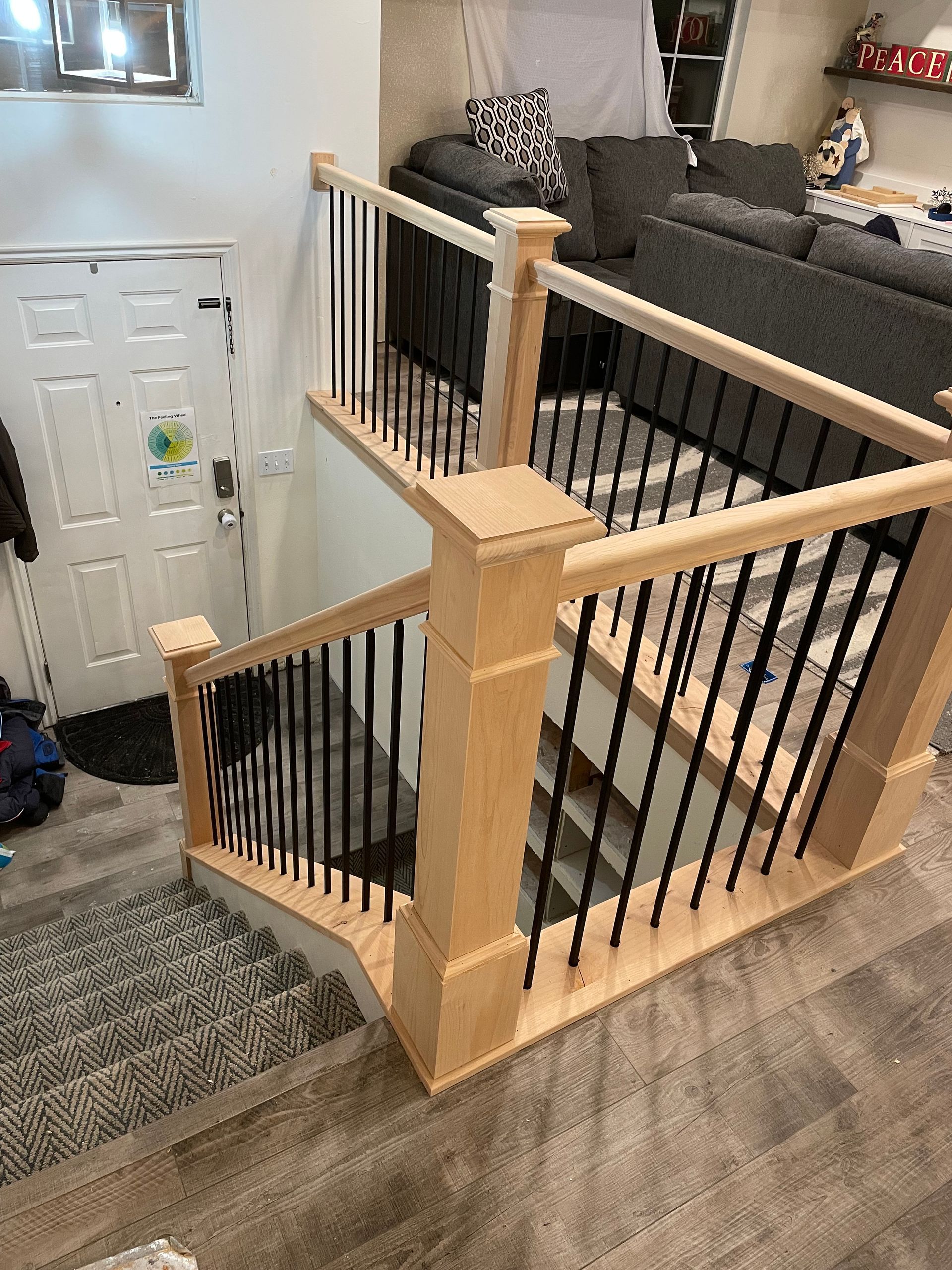 Staircase with light wood and black railings leading down to a lower level with a white door.