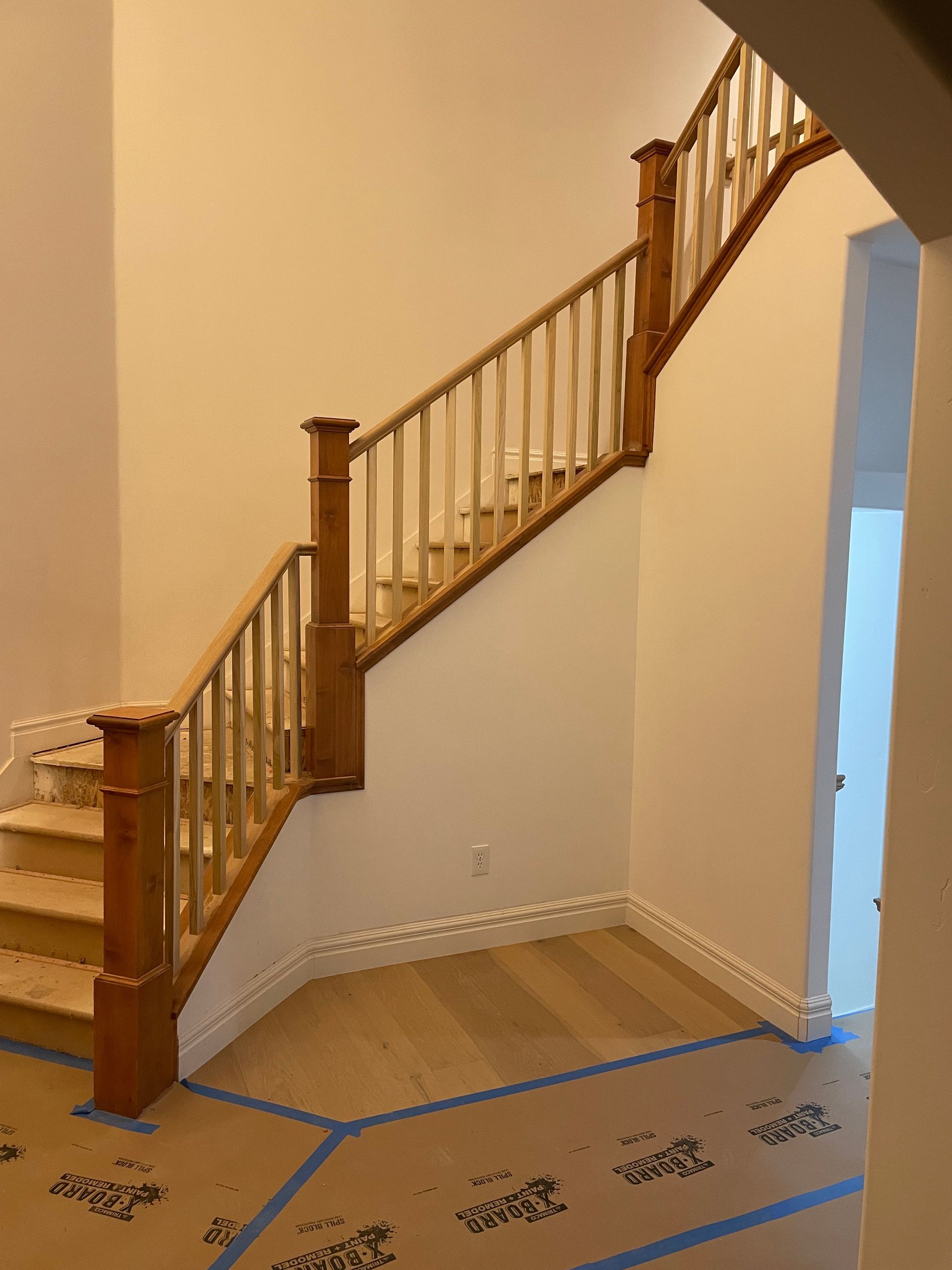 Wooden staircase with light brown railing, light wood steps, and tan walls.