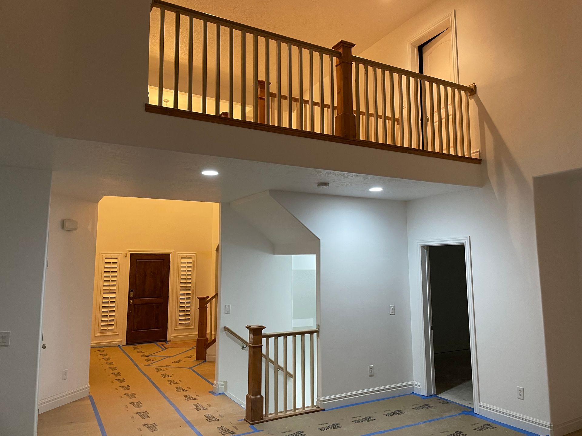 Interior view of a house with a loft, staircase, and doorway. Wooden railing and trim; walls are white.