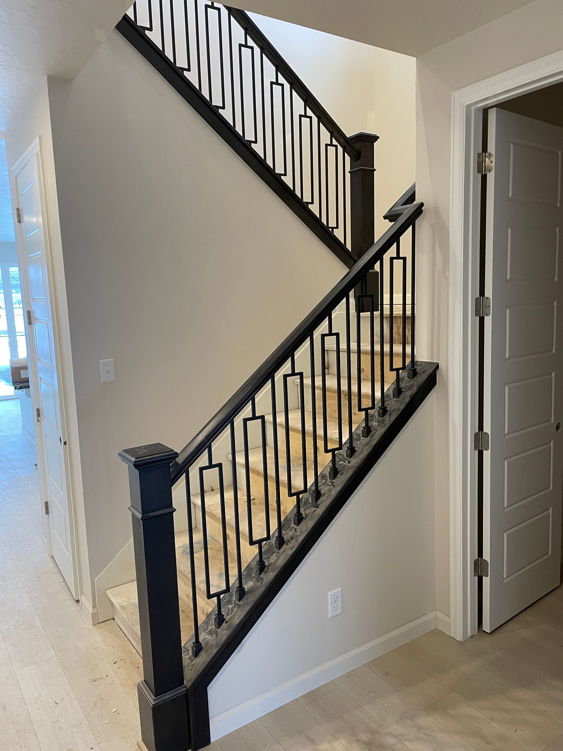 Staircase with black railing and light-colored walls. A door is on the right.