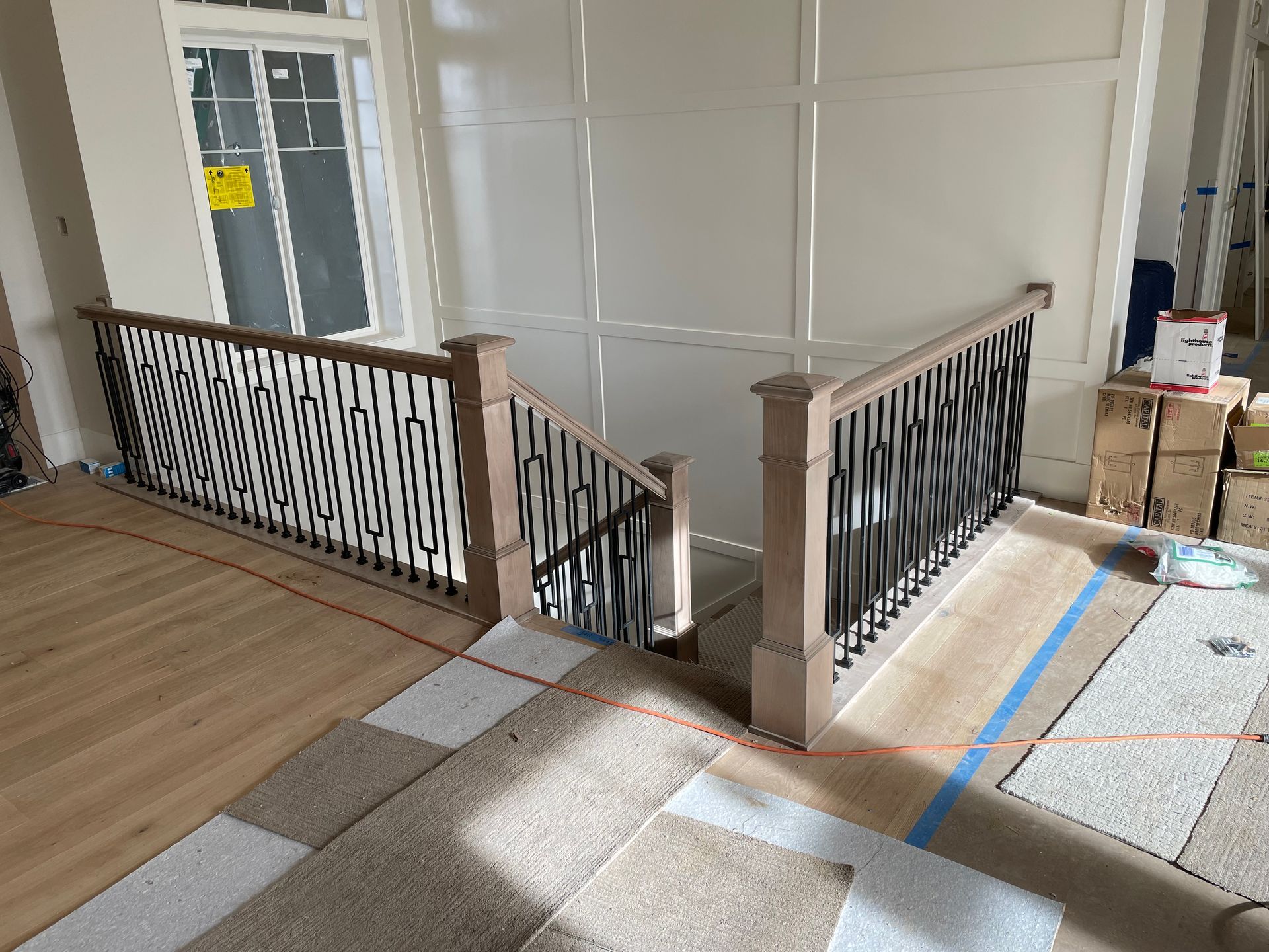 A staircase with wood banisters and black decorative metalwork in a building under construction.