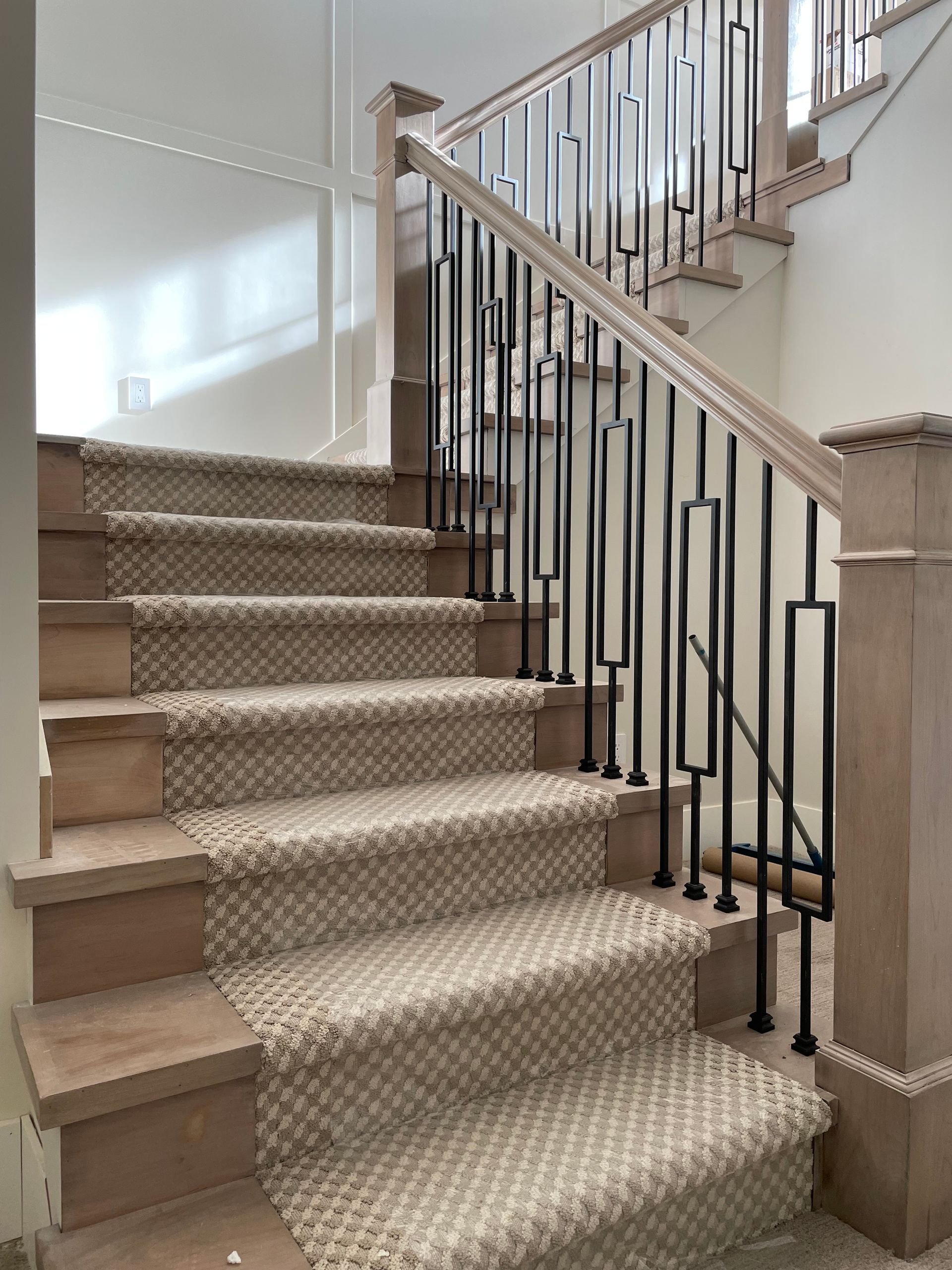 Staircase with light brown steps and carpet, black railing, and wooden posts.