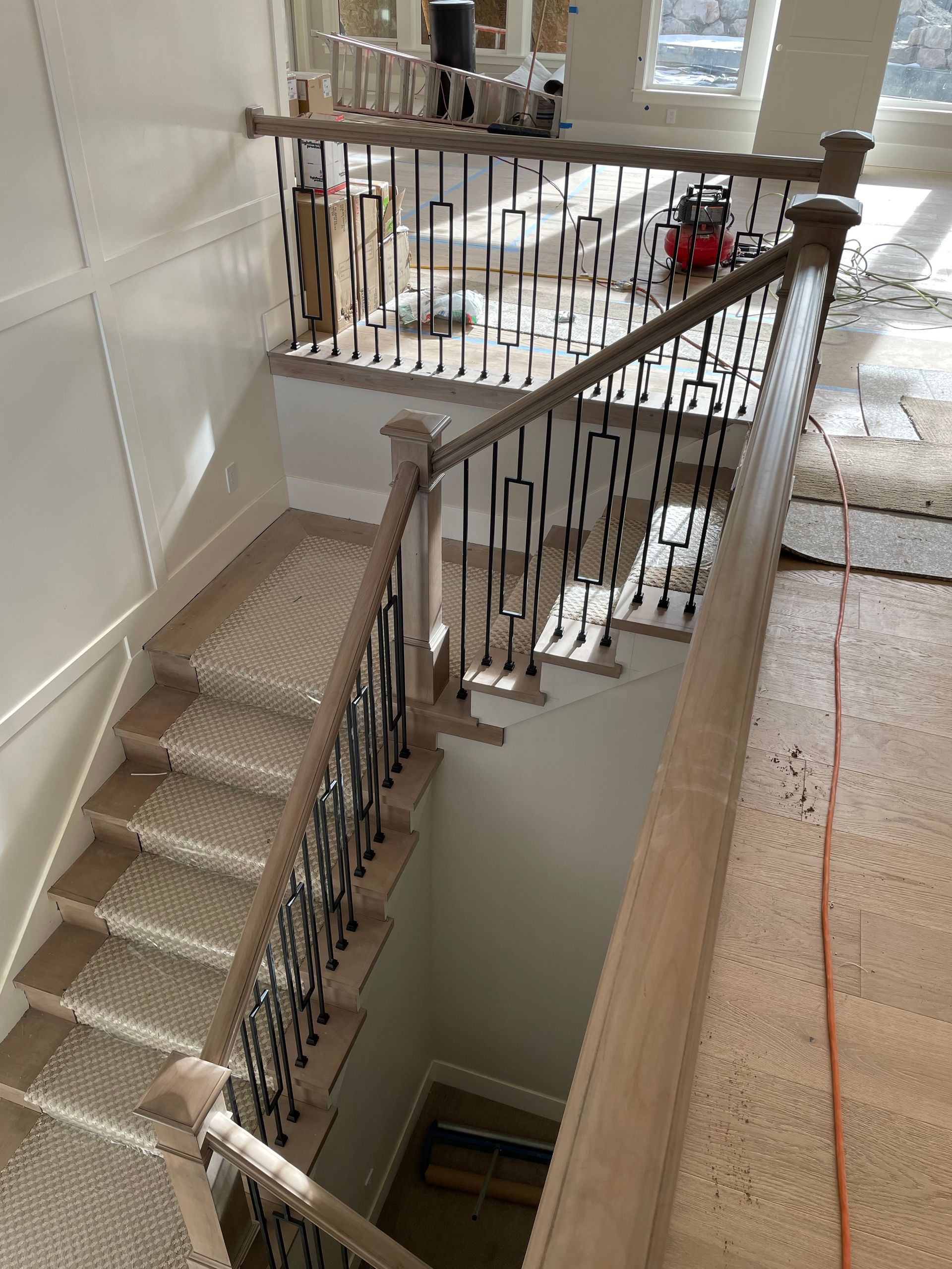 Staircase with wooden handrails and black iron balusters, leading down.  Light wood flooring and wall panels.