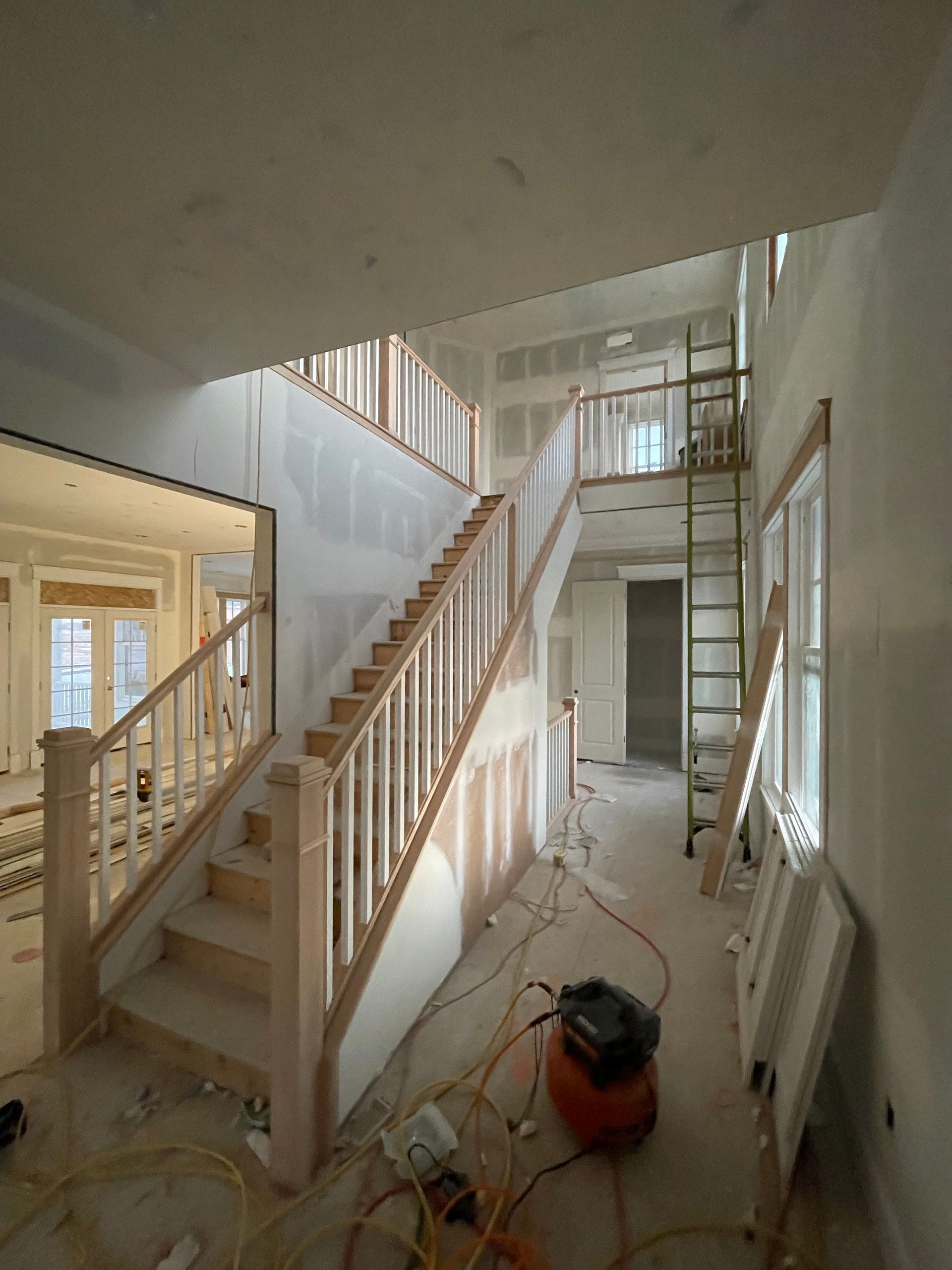 Interior of a house under construction; a staircase with wooden handrails, unfinished walls, and scattered tools.