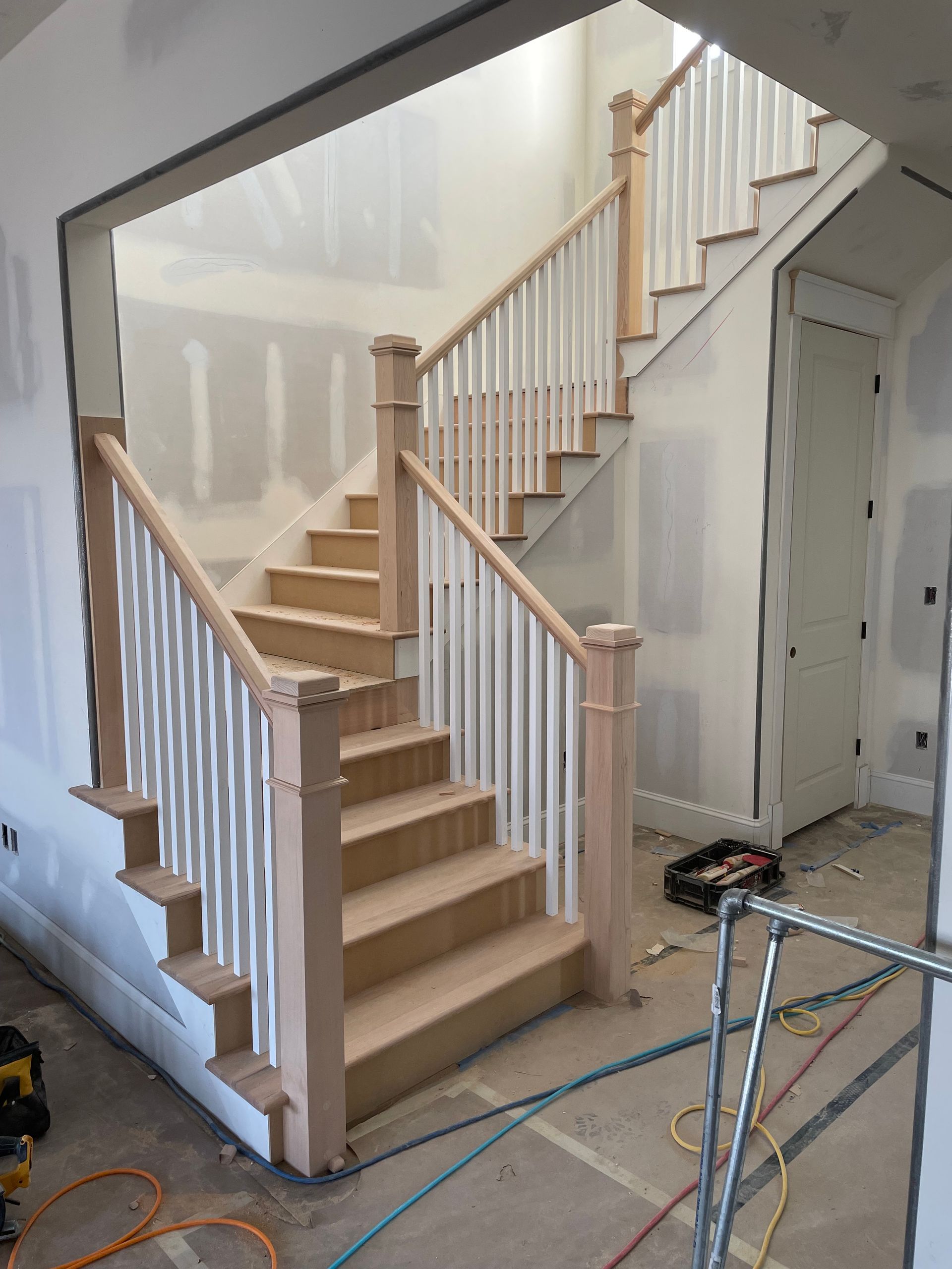 Staircase under construction with wood treads, white balusters, and light-colored railing.