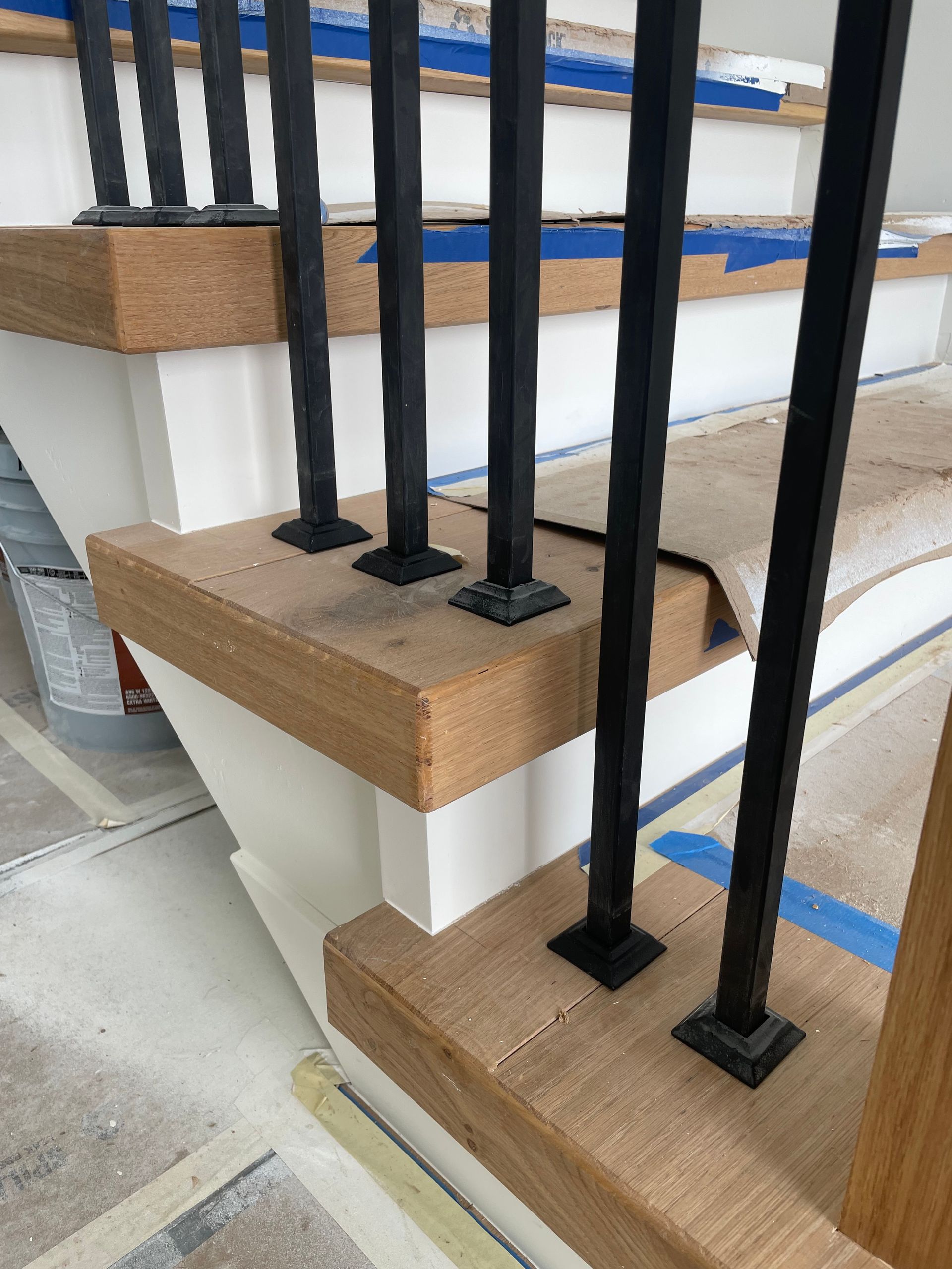 Staircase with black metal balusters on a wooden base, painted white below. Construction in progress.
