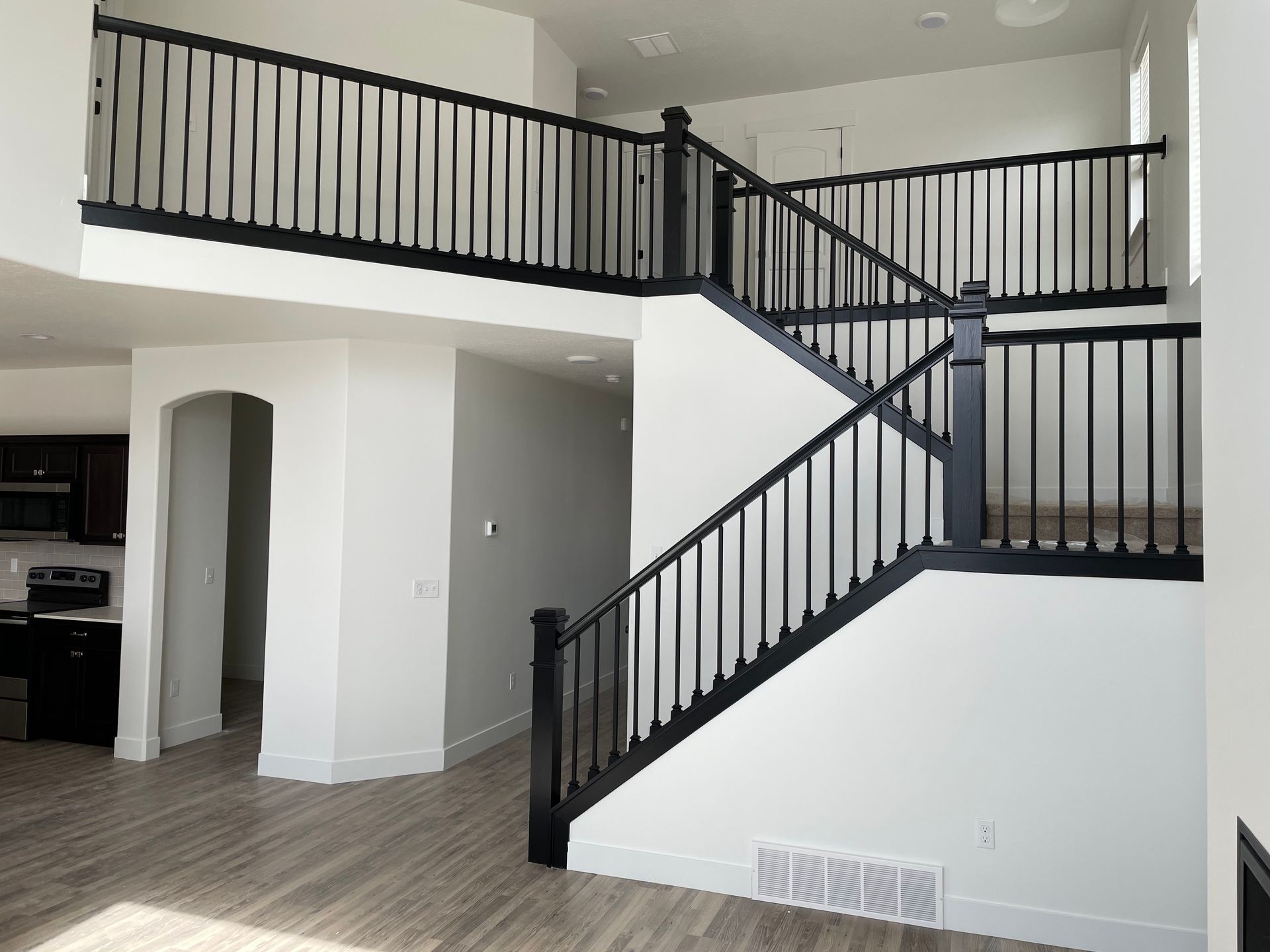 Two-story home interior with a black railing staircase and balcony against white walls.