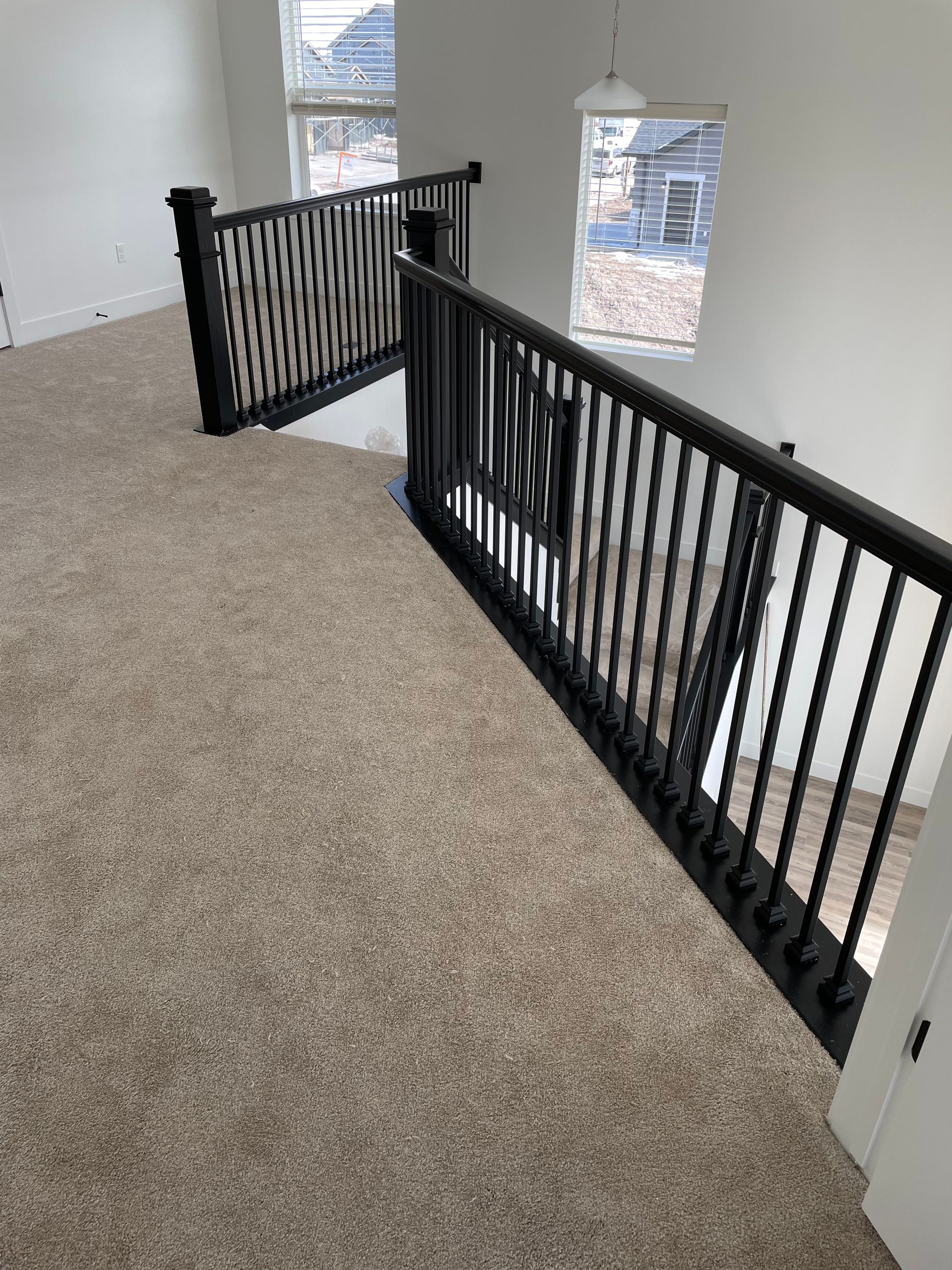 Interior view of a second-story landing with black railing, beige carpet, and white walls.