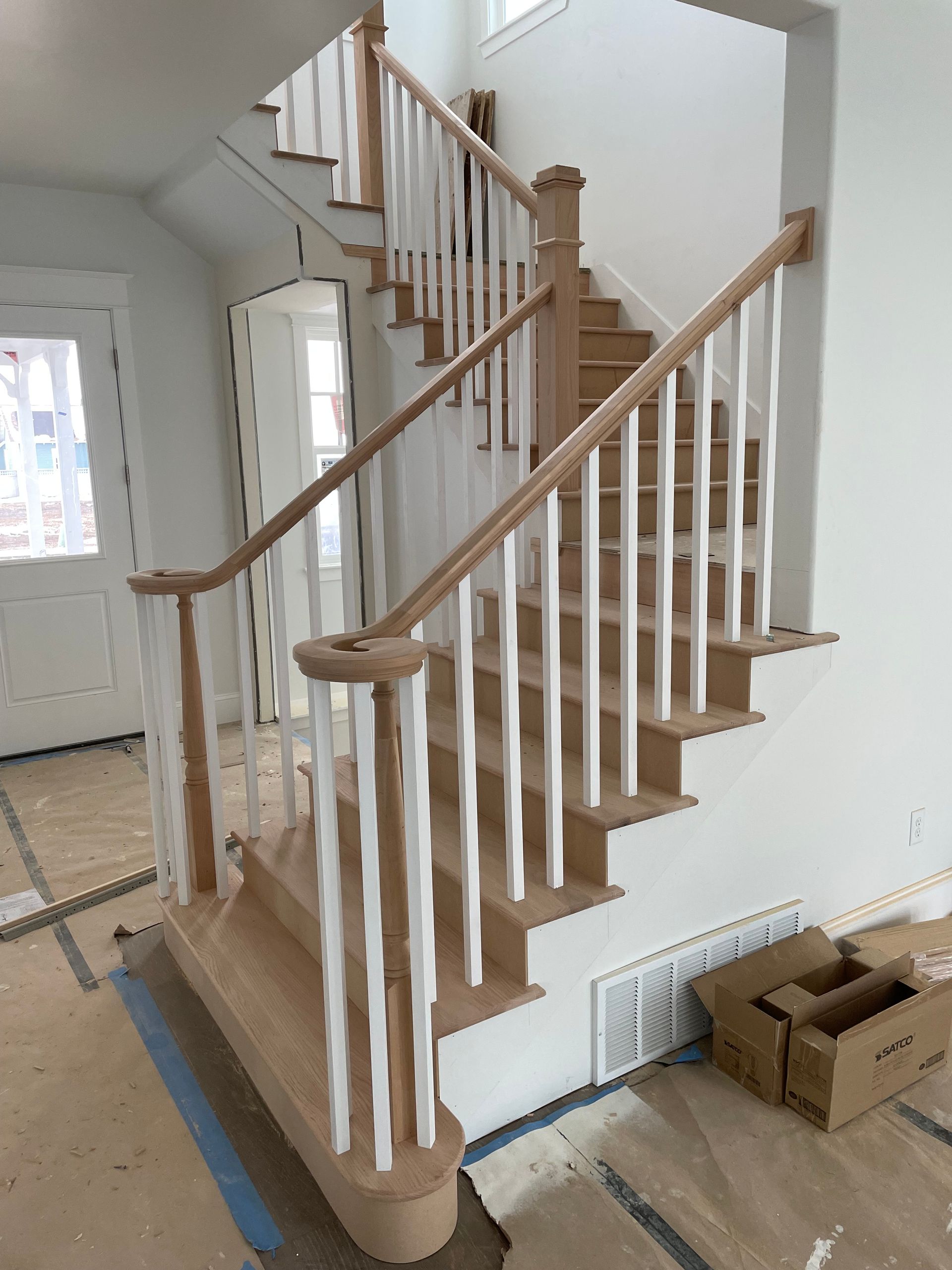 Wooden staircase with white spindles, brown handrails and treads, set in a new construction home.