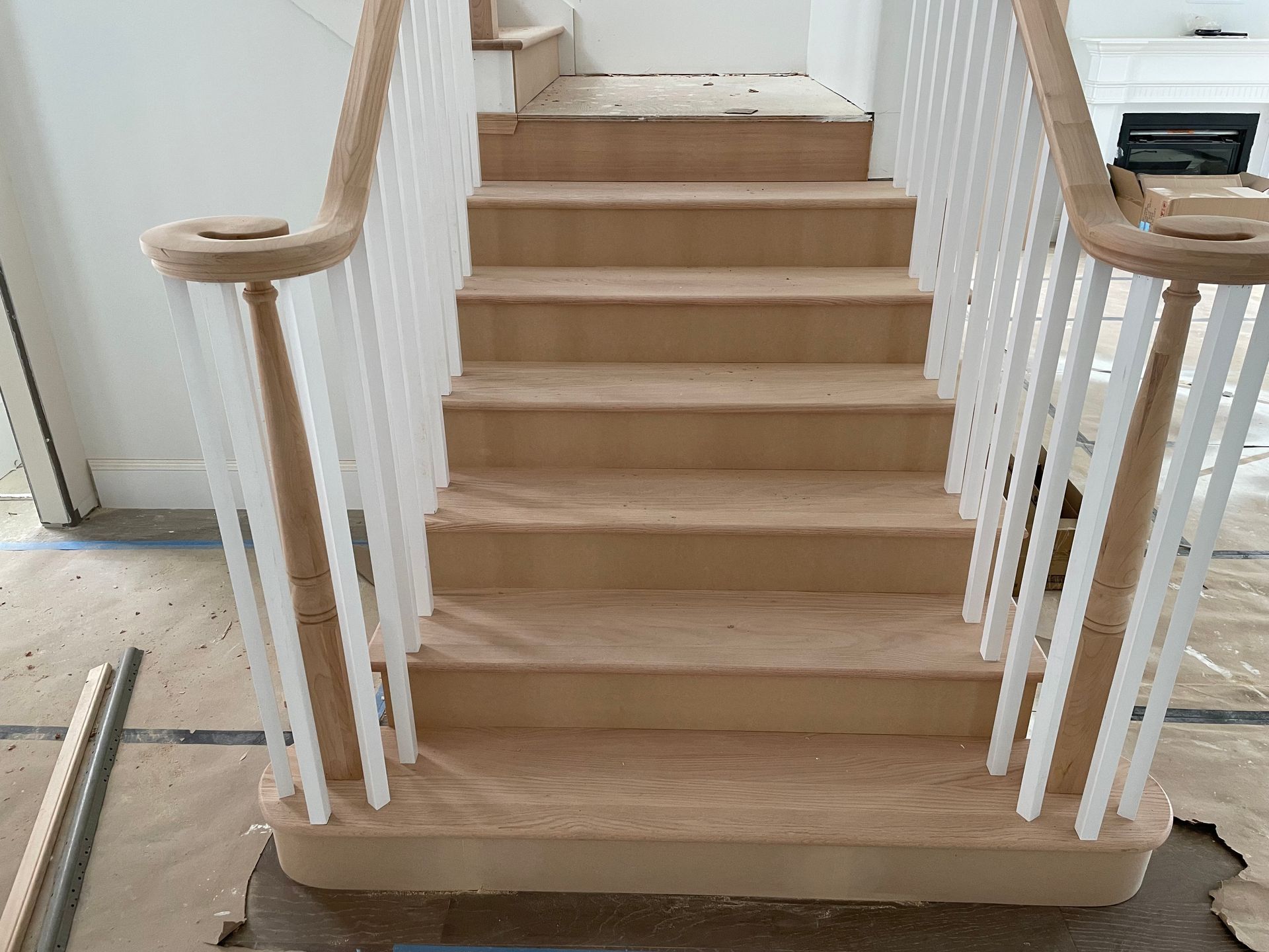 Staircase with light-colored steps and white balusters and handrails; under construction indoors.
