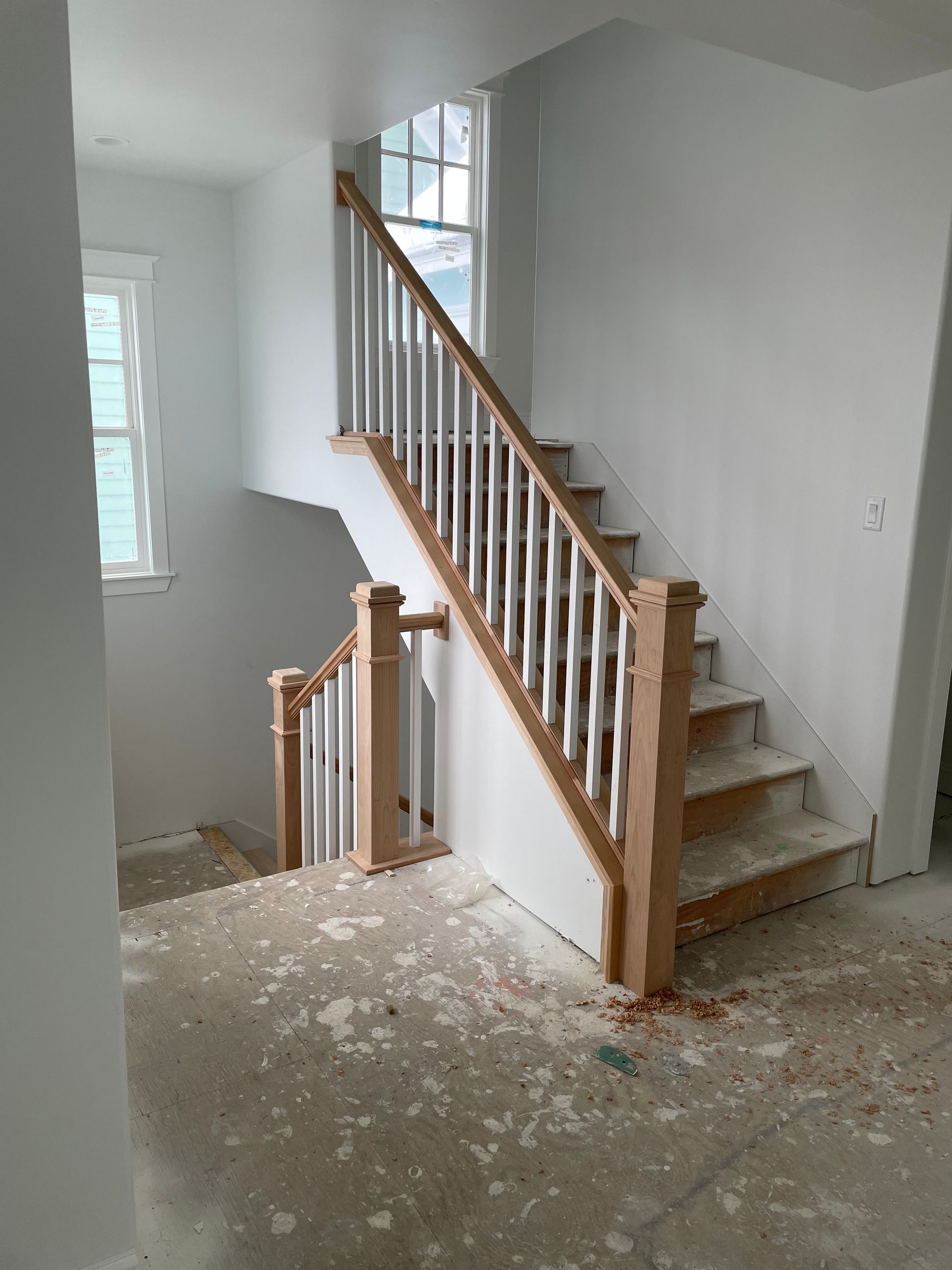 Staircase with light wood railing and white spindles, leading up to a window. Construction debris visible on the floor.