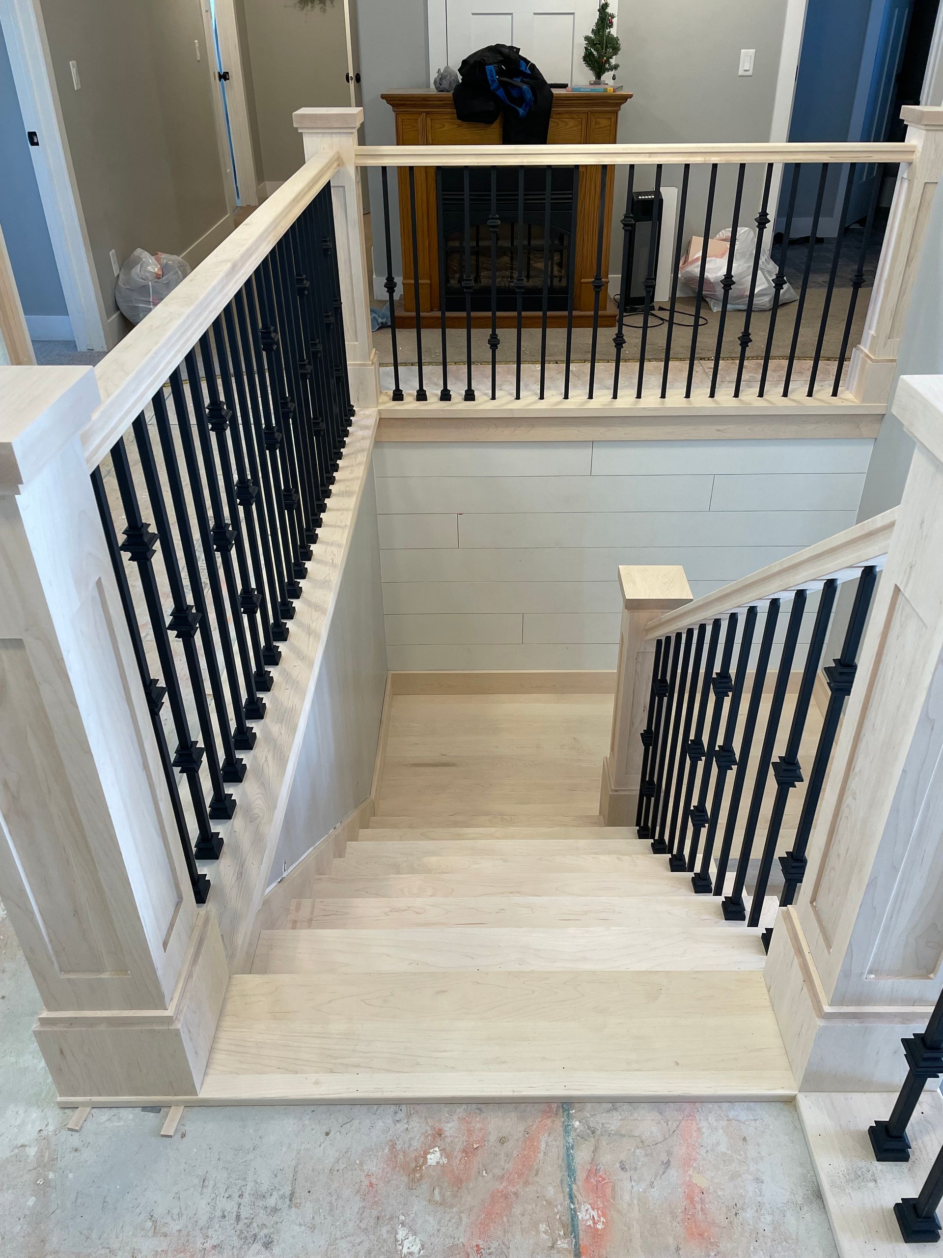 Wooden staircase with black metal balusters, leading down to a lower level with exposed wall.