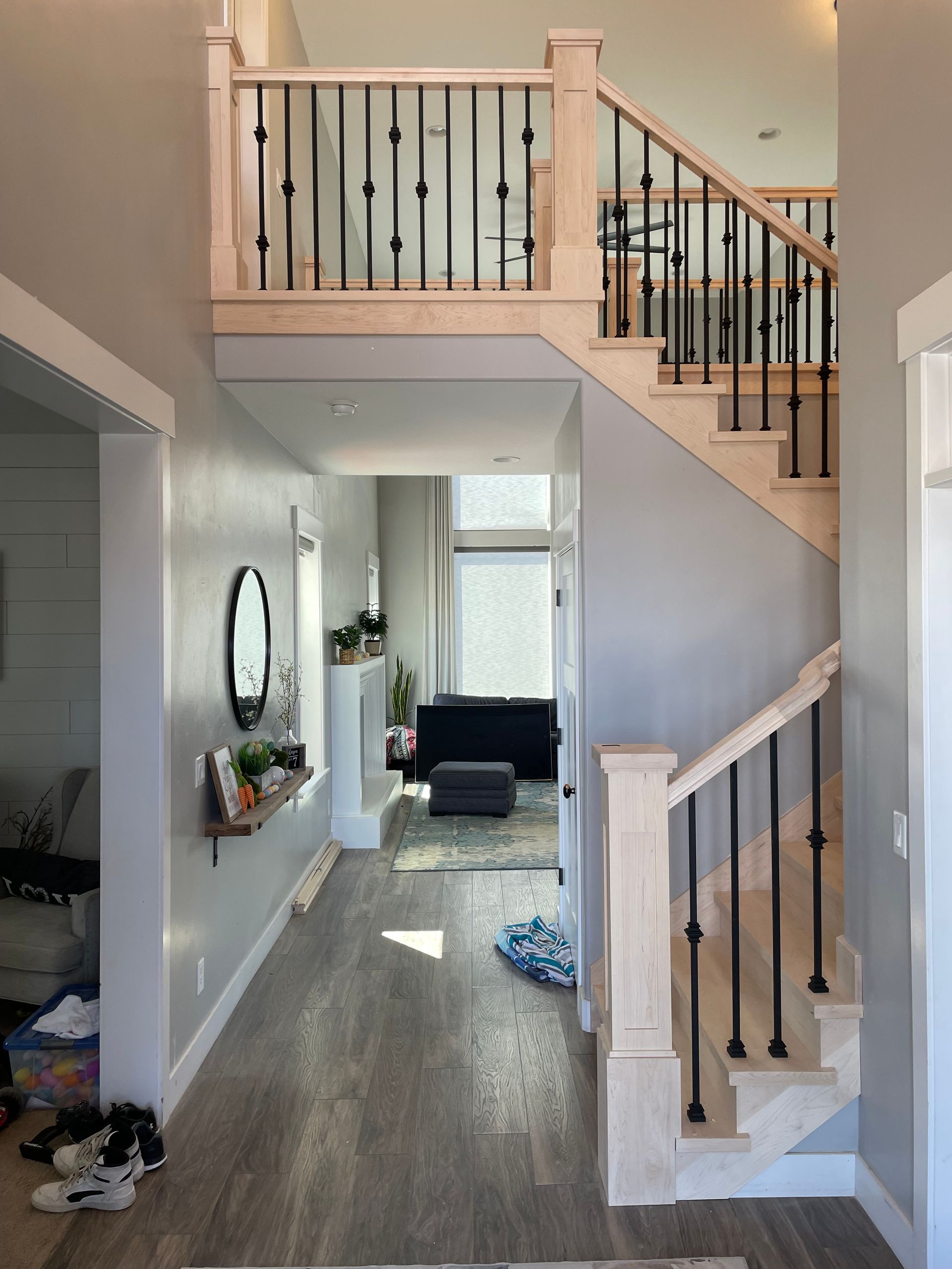 Hallway with stairs and light wood and black metal railing. Gray walls and flooring.
