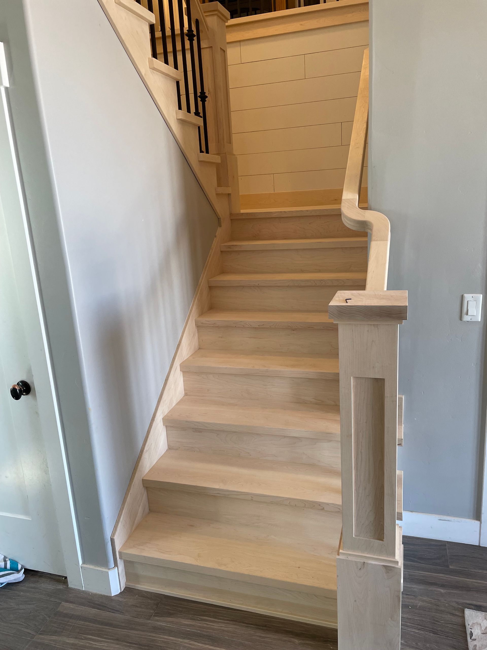 Staircase with light wood steps, white balustrade, black iron railing, gray walls.