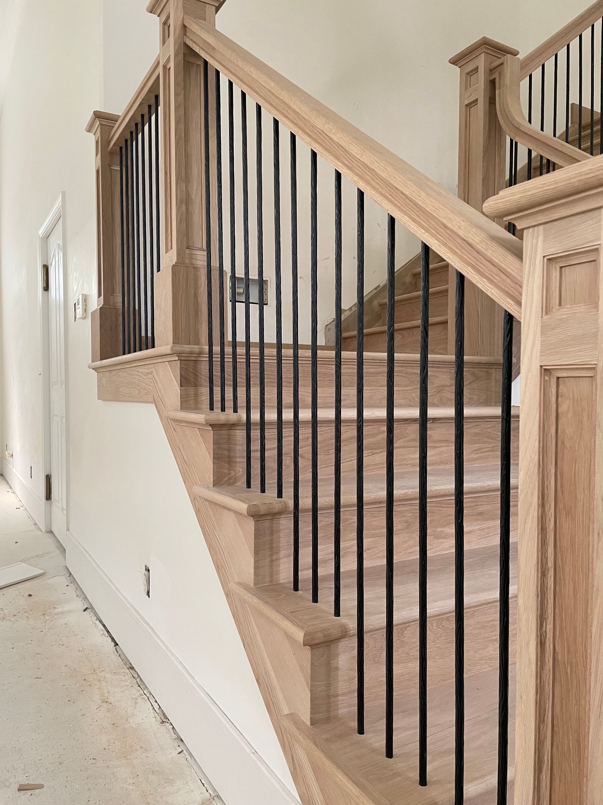 Staircase with wooden steps, a white wall, and black vertical bars for railing.