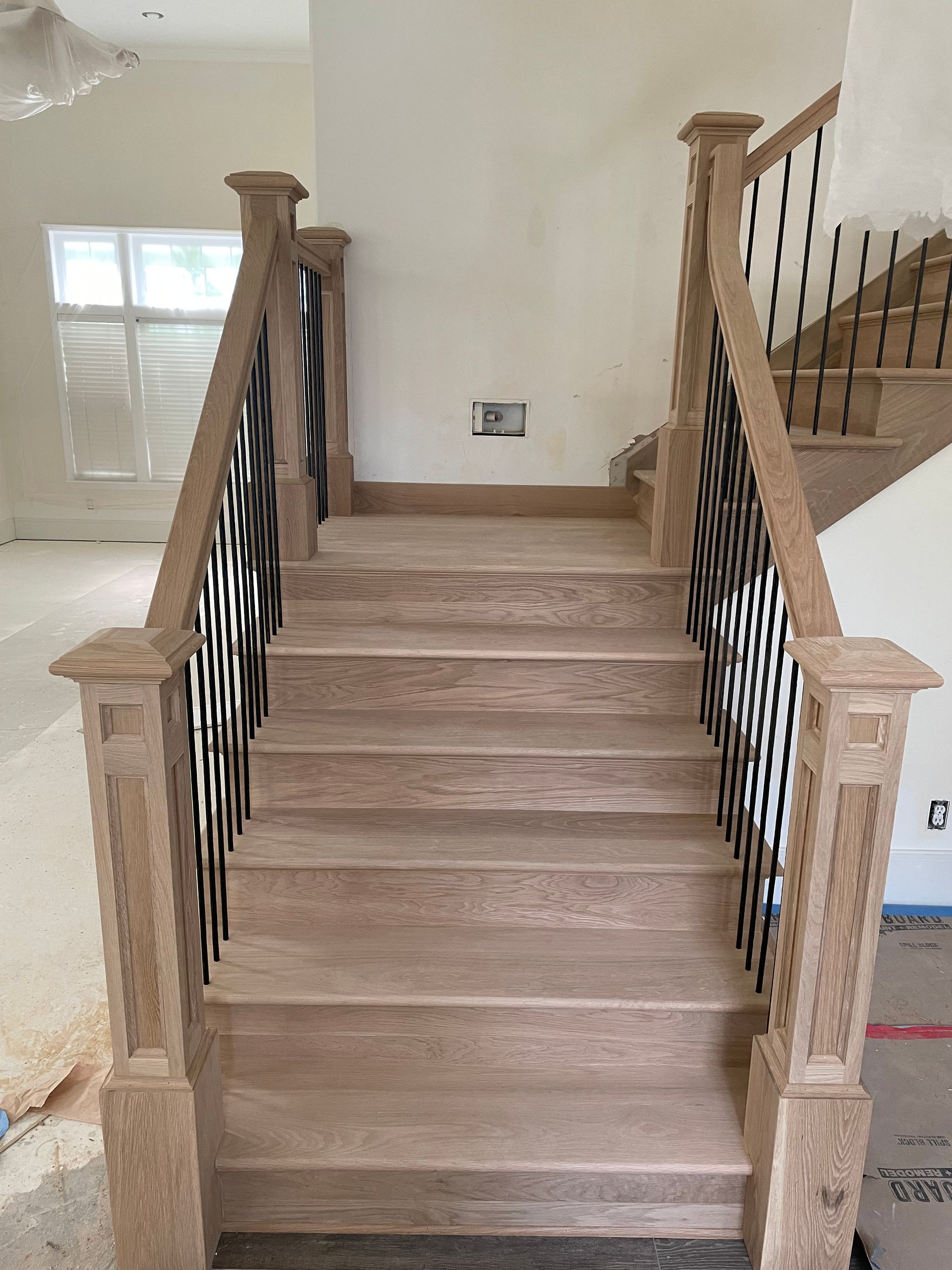 Wooden staircase with black iron balusters, natural light, and beige walls.