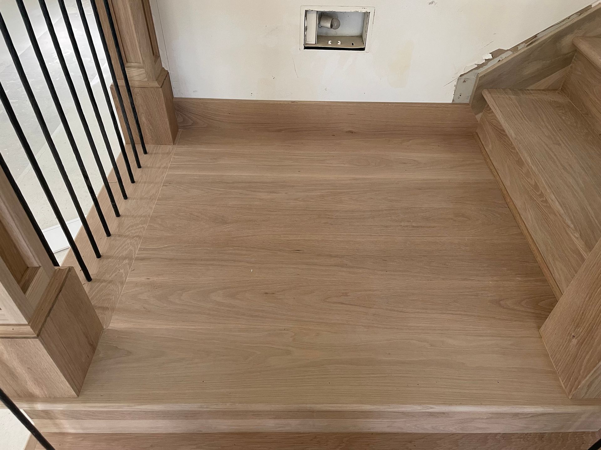 Wooden staircase landing with black metal railings and unfinished walls.
