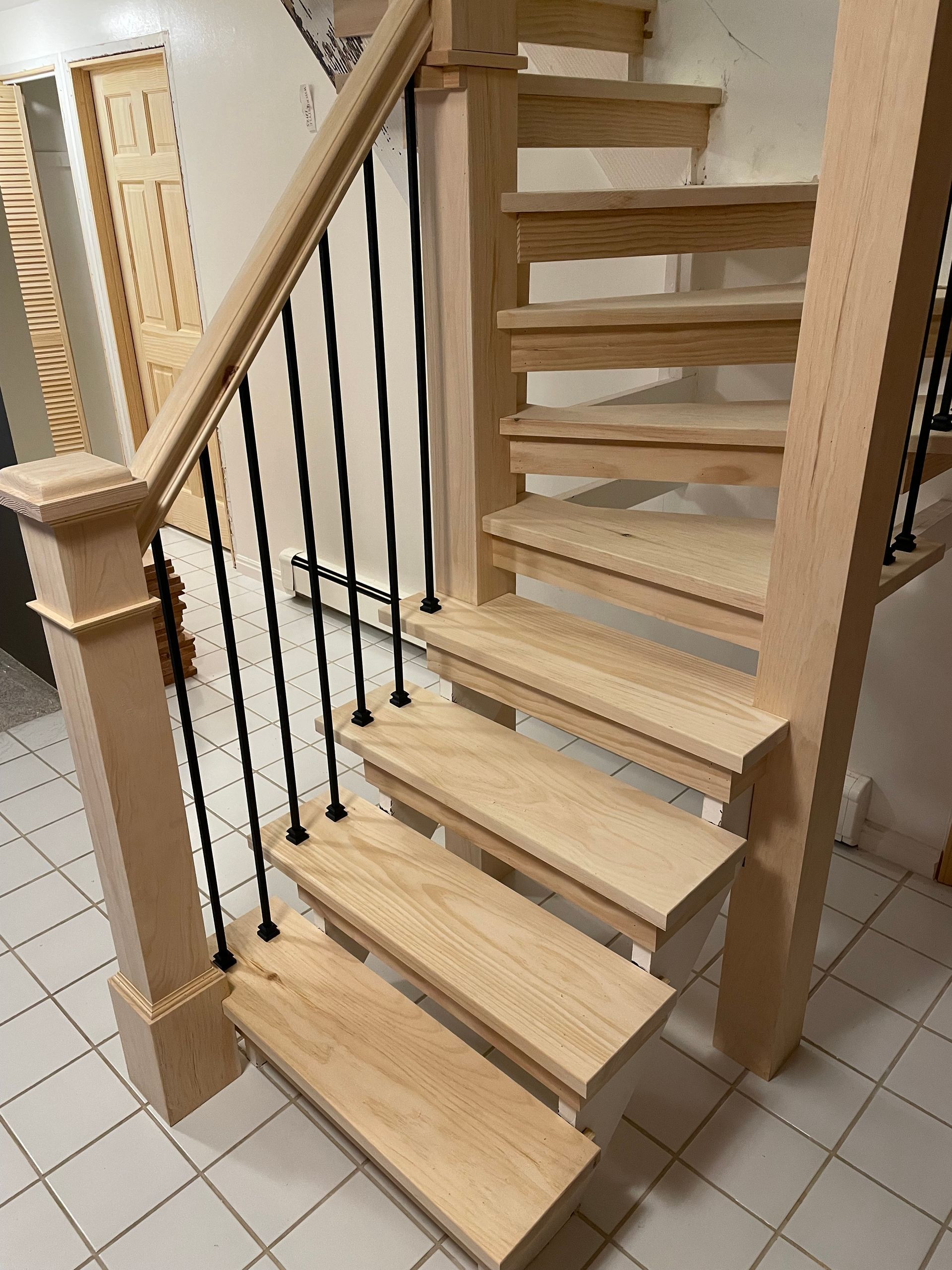 Wooden staircase with black metal balusters, natural wood finish, and tiled floor.