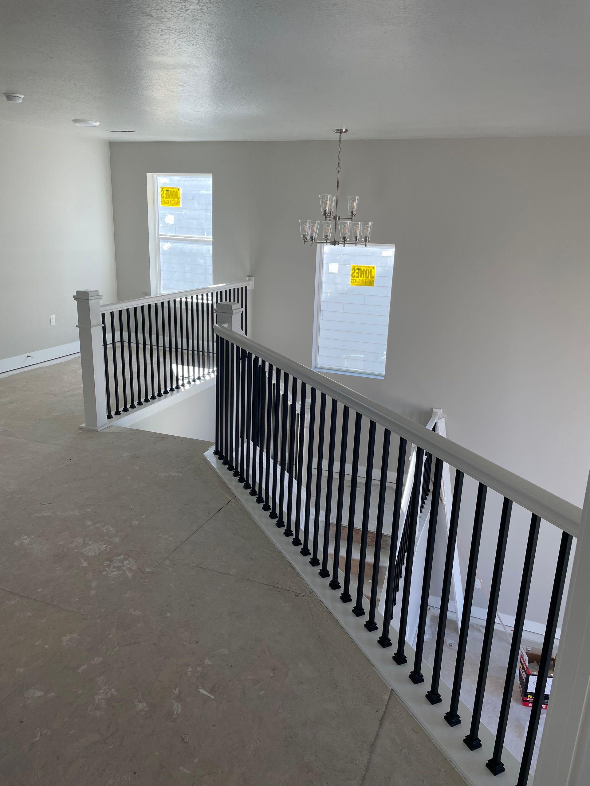 Interior view of a second-floor hallway with white railing and black spindles, light fixtures, and a window.