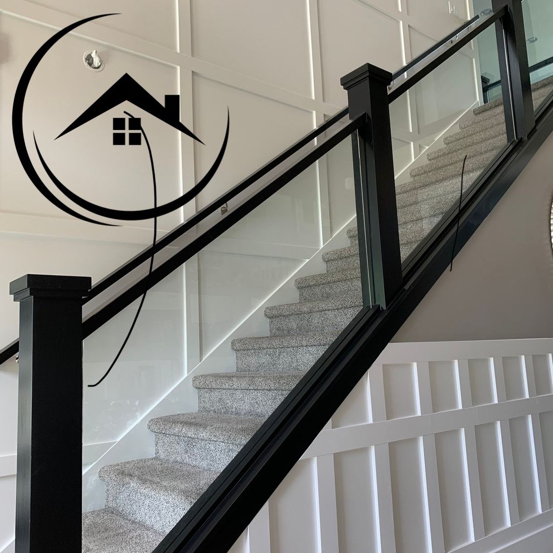 Staircase with black banister, clear glass panels, and patterned carpet. White paneled walls.