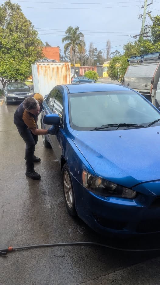 A person washes a blue car outdoors — ATD Automotive in North Wollongong, NSW