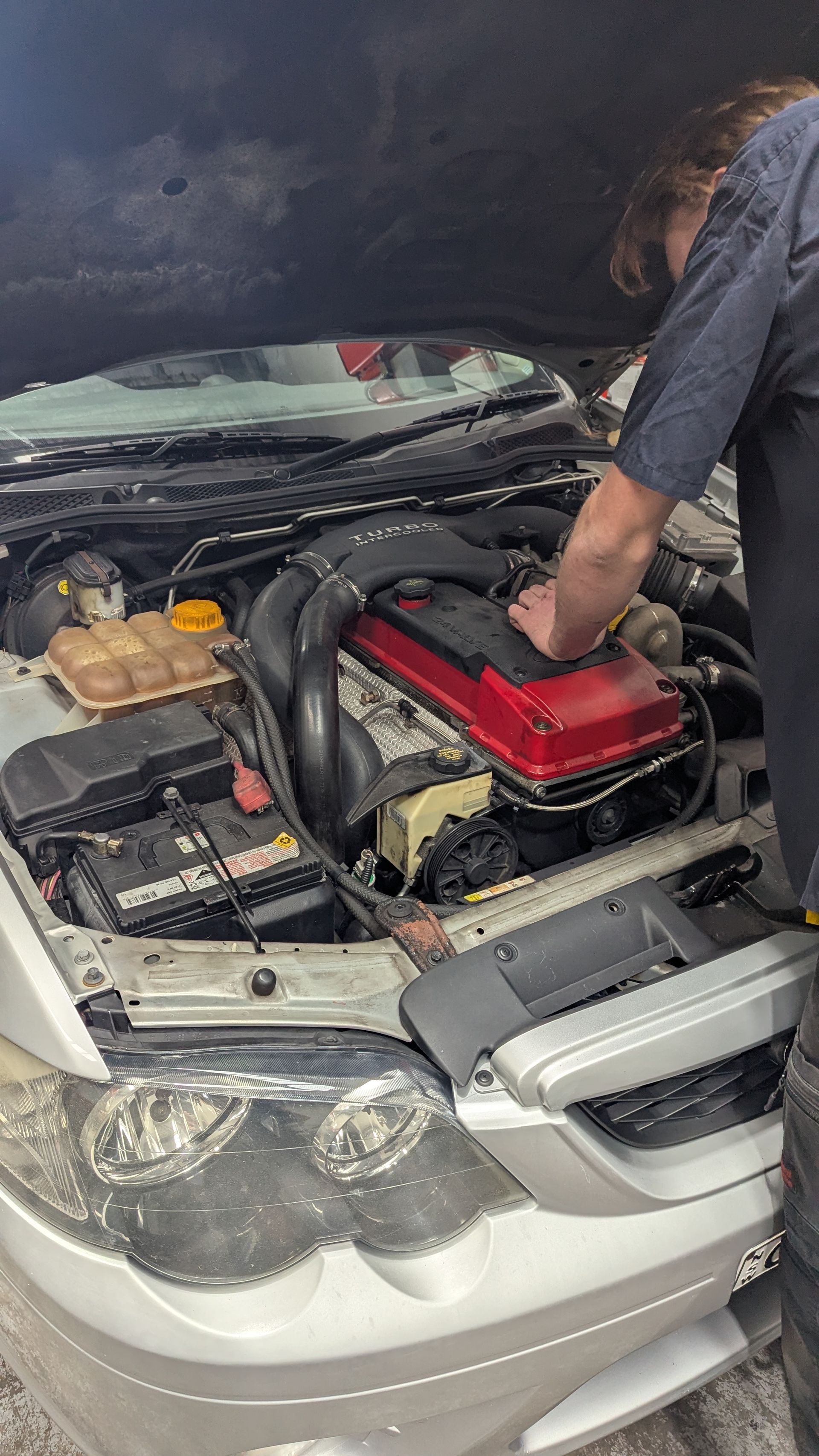 A person working on a car engine, a red cover visible, in an automotive setting — ATD Automotive in North Wollongong, NSW