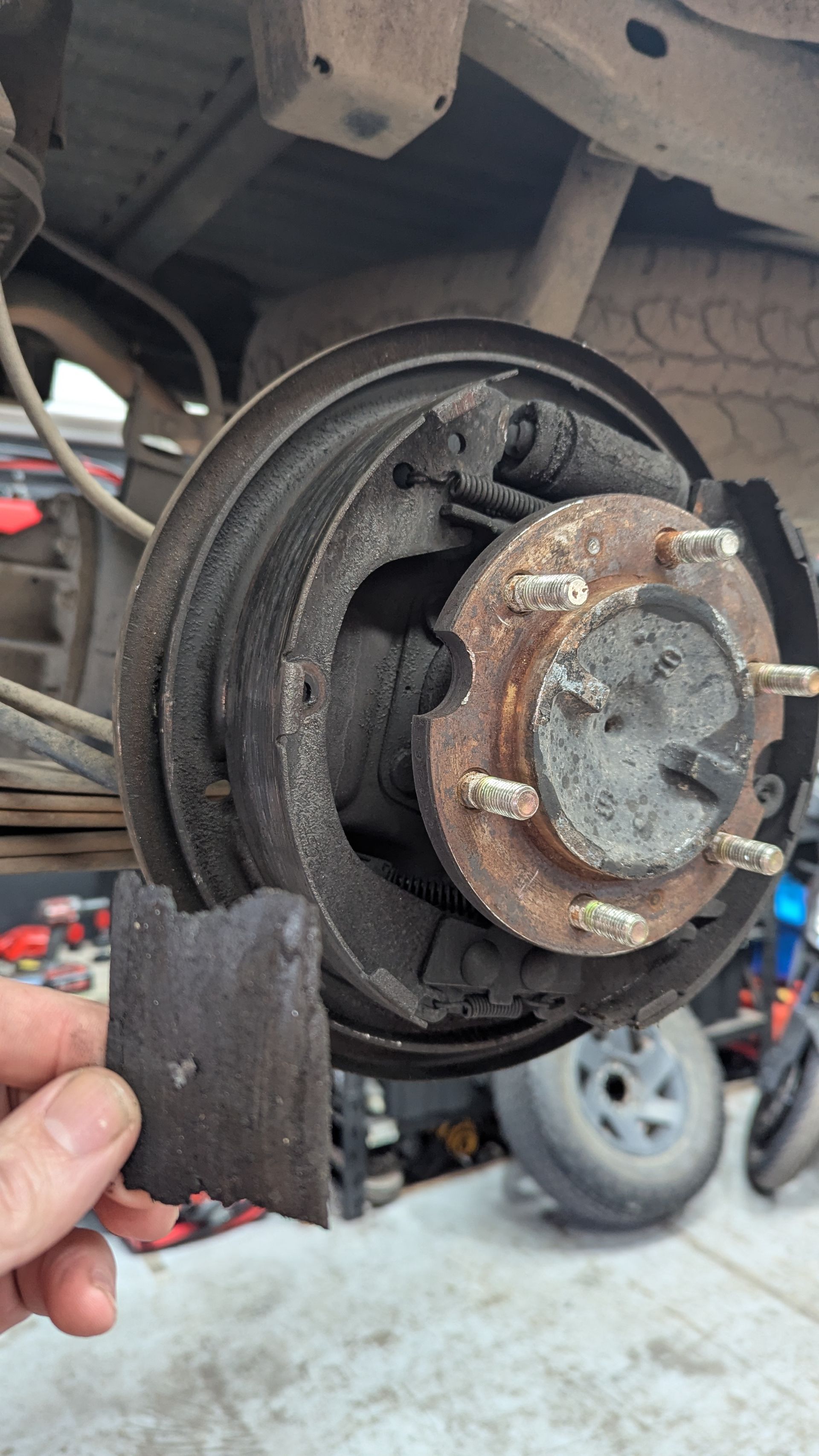 Hand holding a broken brake pad fragment in front of a truck's exposed brake drum, showing wear and tear — ATD Automotive in North Wollongong, NSW